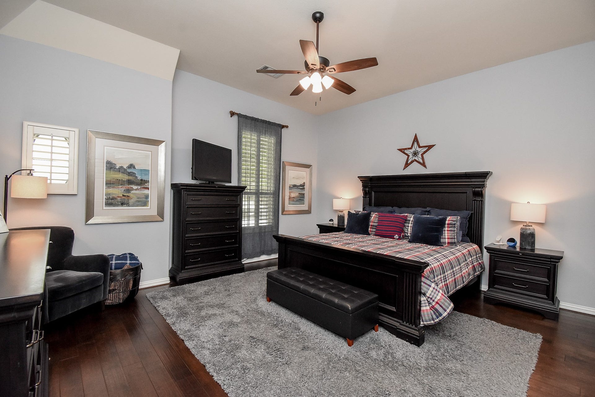 Large primary suite with wood flooring, ceiling fan and custom shutters.