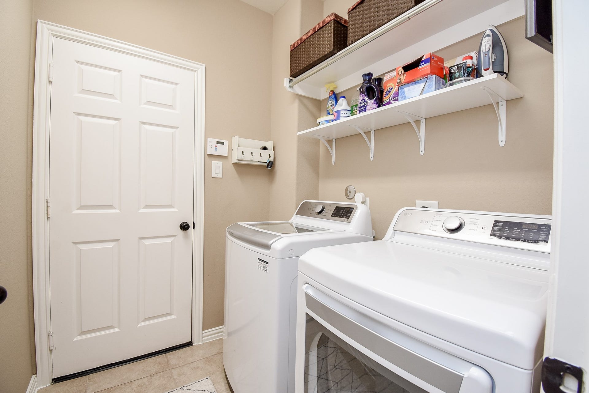 Laundry room with plenty of shelving/storage. Door leads into epoxy floored double garage.