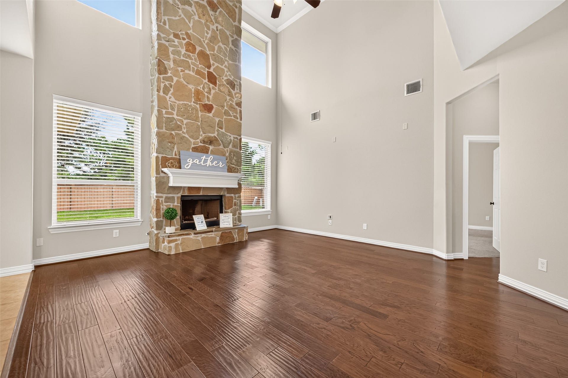 Family room with stone fireplace, tall ceilings and engineered wood floors