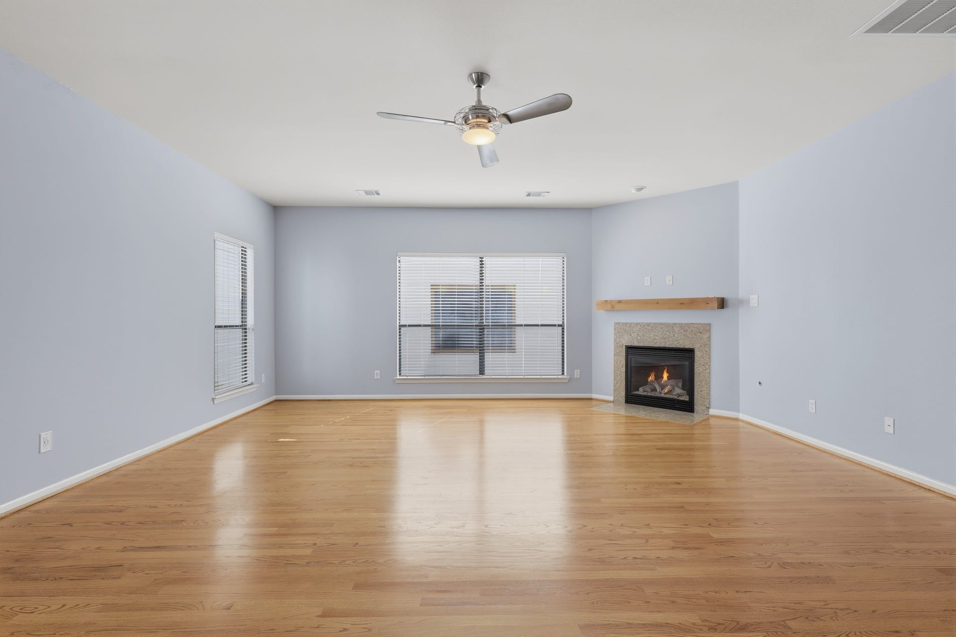 The living area features large windows that fill the space with natural light, hardwood floors, and a working fireplace positioned in the corner.
