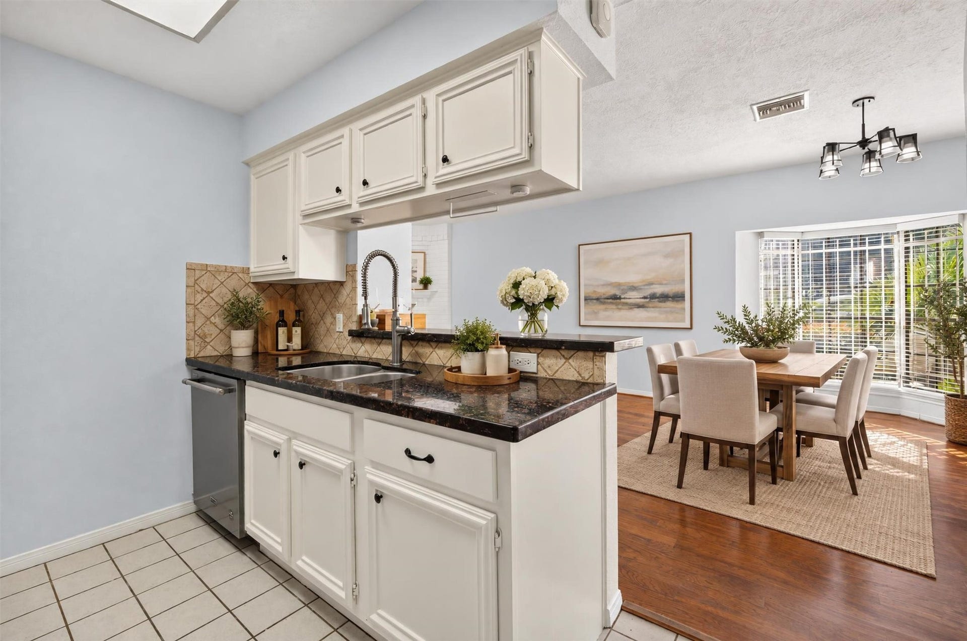 2220 Bering Drive, #12, Houston, TX 77057 Bright kitchen with white cabinetry, granite countertops, a stainless steel dishwasher, and a breakfast bar opening to a sunlit dining area with a bay window. Virtually staged.