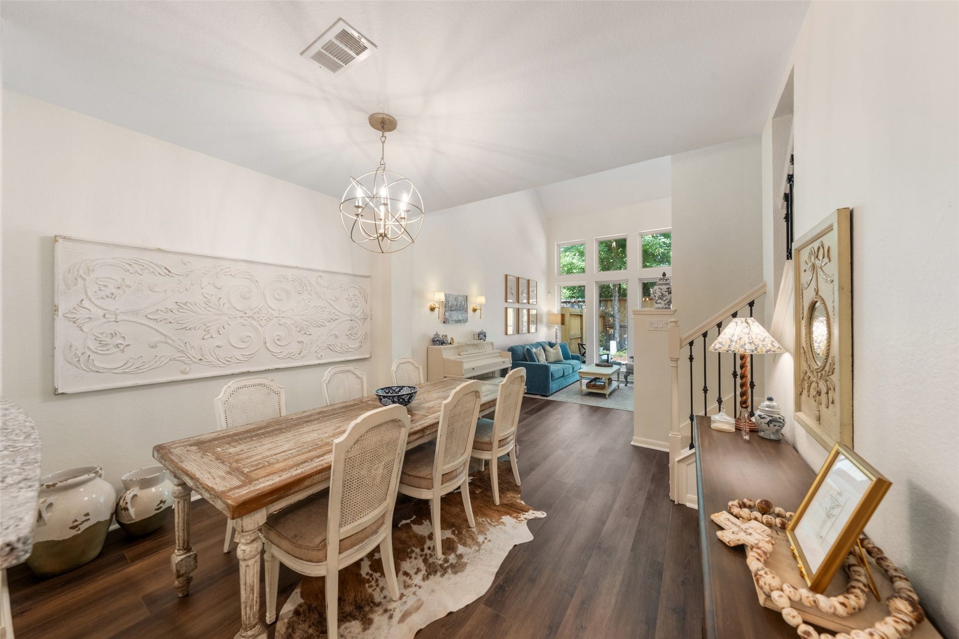 34 Alderon Woods Place, The Woodlands, TX 77382 Elegant dining area with a rustic wooden table and chic chandelier leads into a cozy living space with large windows and abundant natural light.