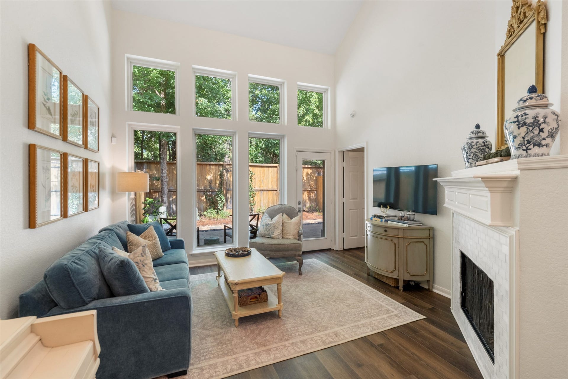 34 Alderon Woods Place, The Woodlands, TX 77382 Bright and inviting living room with high ceilings and expansive windows, offering views of the lush backyard. A cozy fireplace and elegant decor create a warm atmosphere, perfect for relaxation and entertaining.