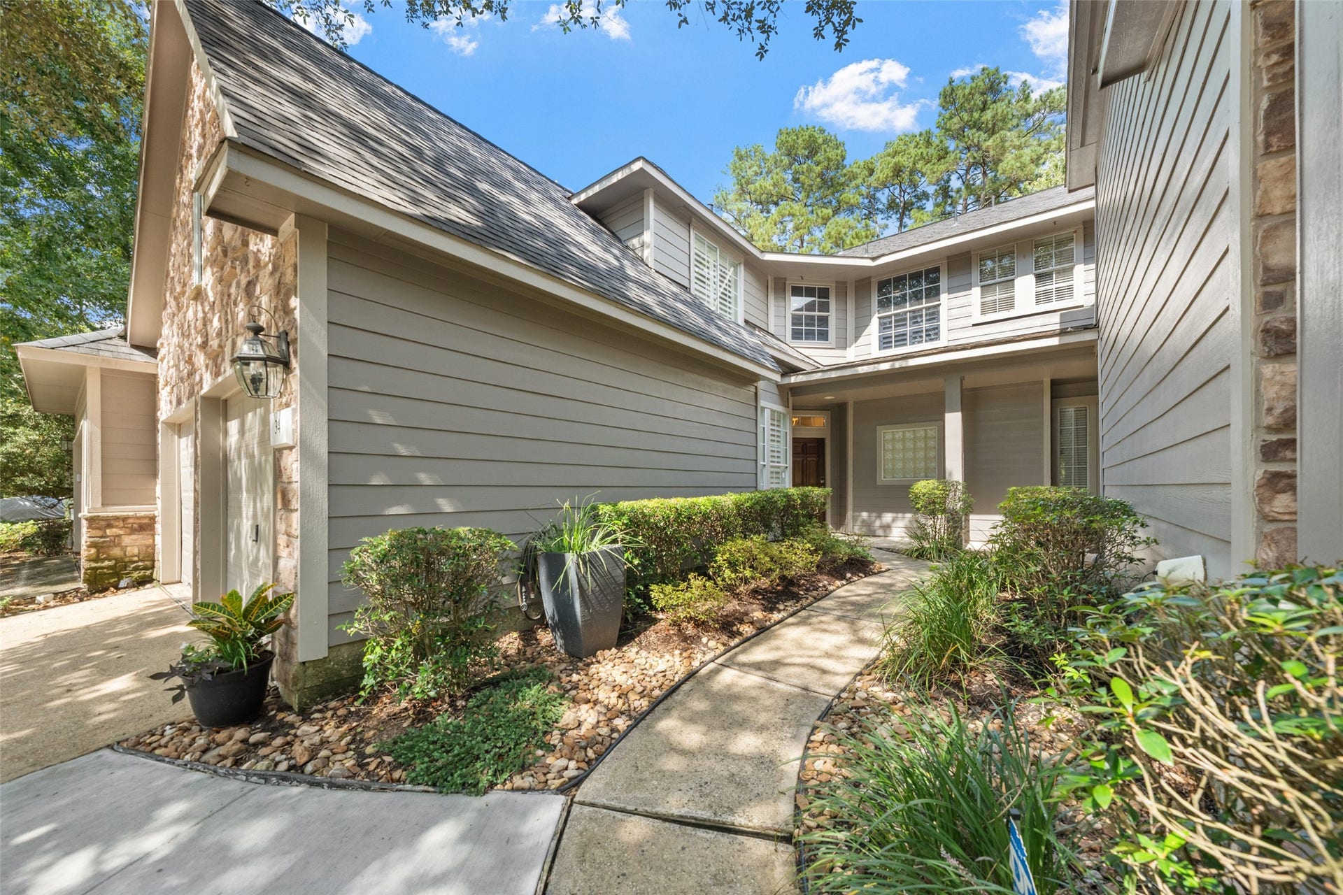 34 Alderon Woods Place, The Woodlands, TX 77382 Charming two-story home with a welcoming walkway, manicured landscaping, and elegant stone accents, nestled in a serene wooded setting.