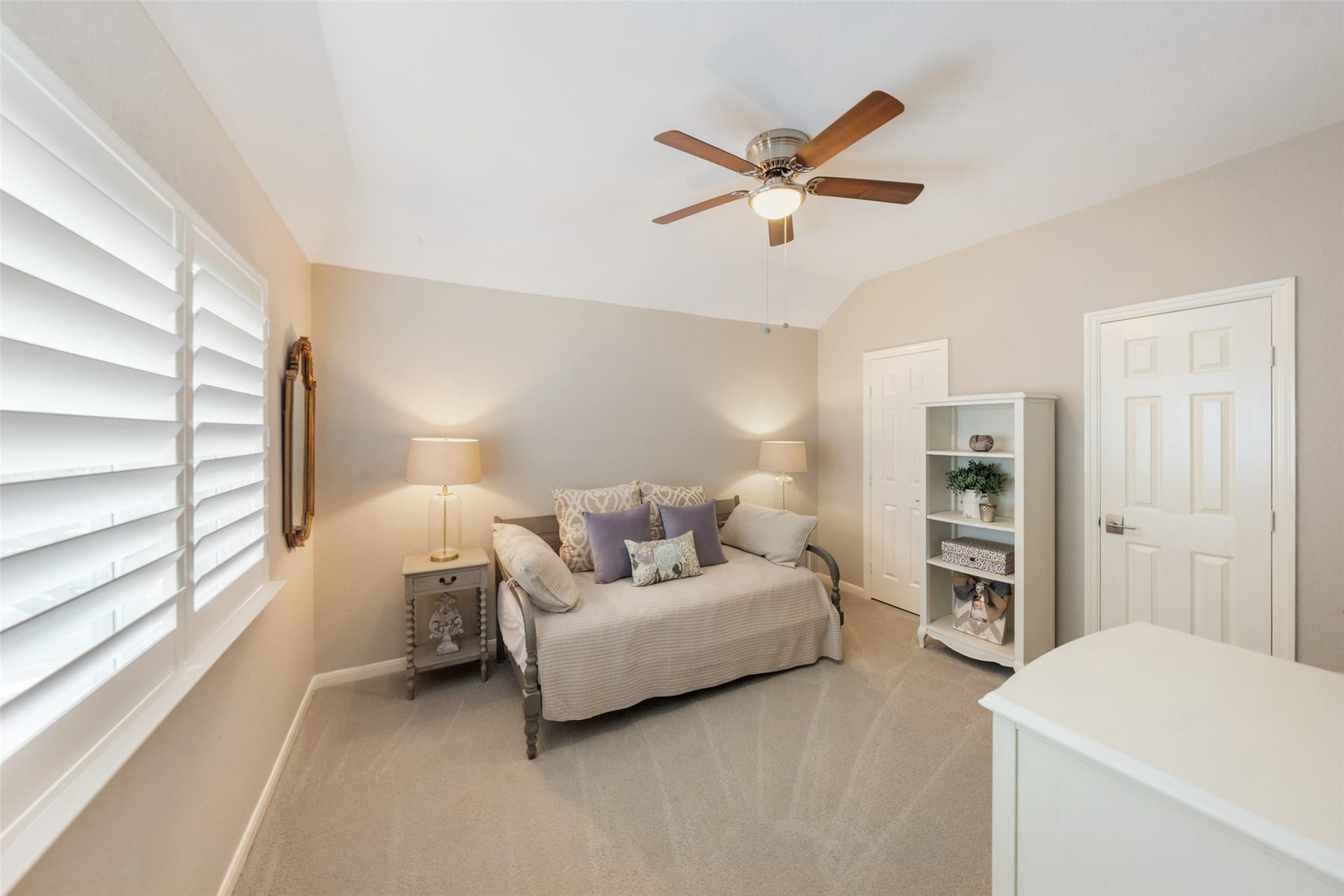 34 Alderon Woods Place, The Woodlands, TX 77382 Cozy secondary bedroom with soft neutral tones, featuring a ceiling fan, plush carpeting, and ample natural light from shuttered windows.