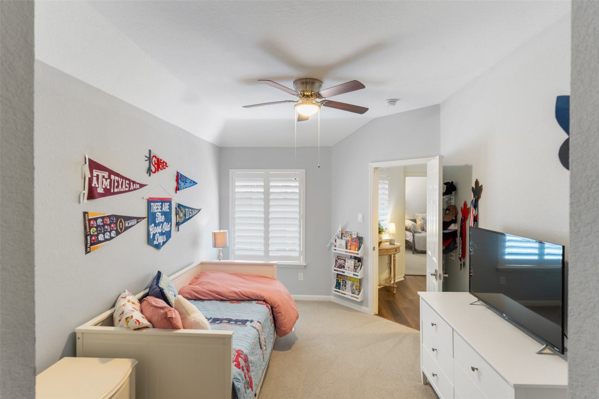 34 Alderon Woods Place, The Woodlands, TX 77382 Charming bedroom with cozy carpeting and soft gray walls, featuring a ceiling fan for comfort. it offers ample space with a dresser and a bed, leading to an adjoining room addition that adds tons of room and endless possibilities.