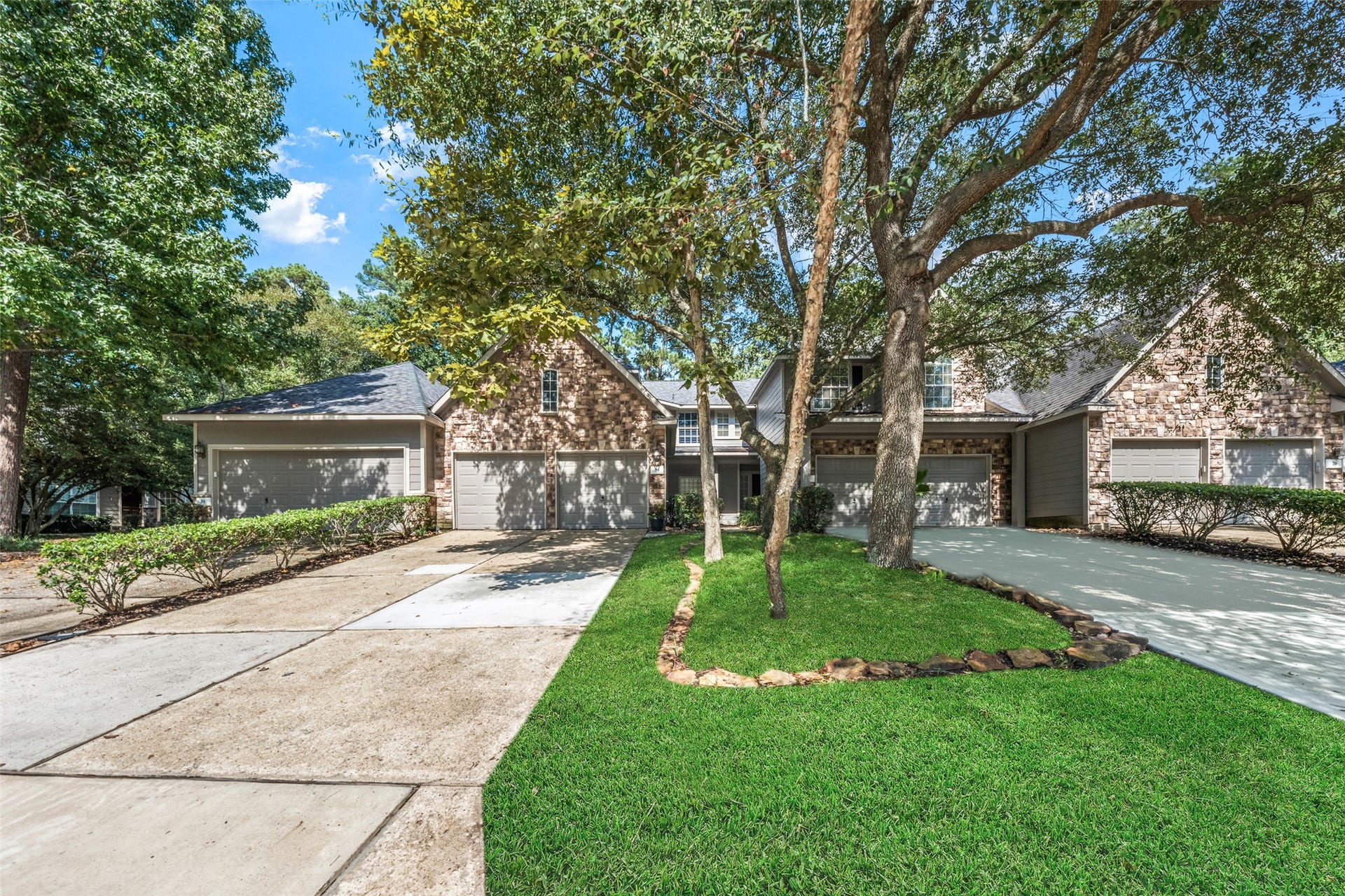 34 Alderon Woods Place, The Woodlands, TX 77382 Charming brick townhouse with a spacious two-car garage, nestled among mature trees and lush landscaping for serene curb appeal.