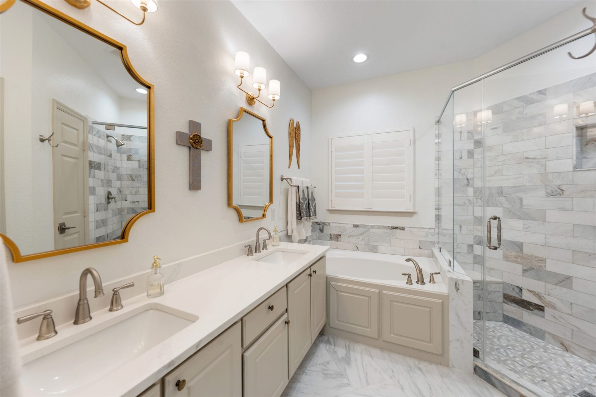 34 Alderon Woods Place, The Woodlands, TX 77382 Elegant primary bathroom featuring a spacious double vanity with chic mirrors, a luxurious soaking tub, and a glass-enclosed marble shower, all enhanced by soft lighting and stylish fixtures.