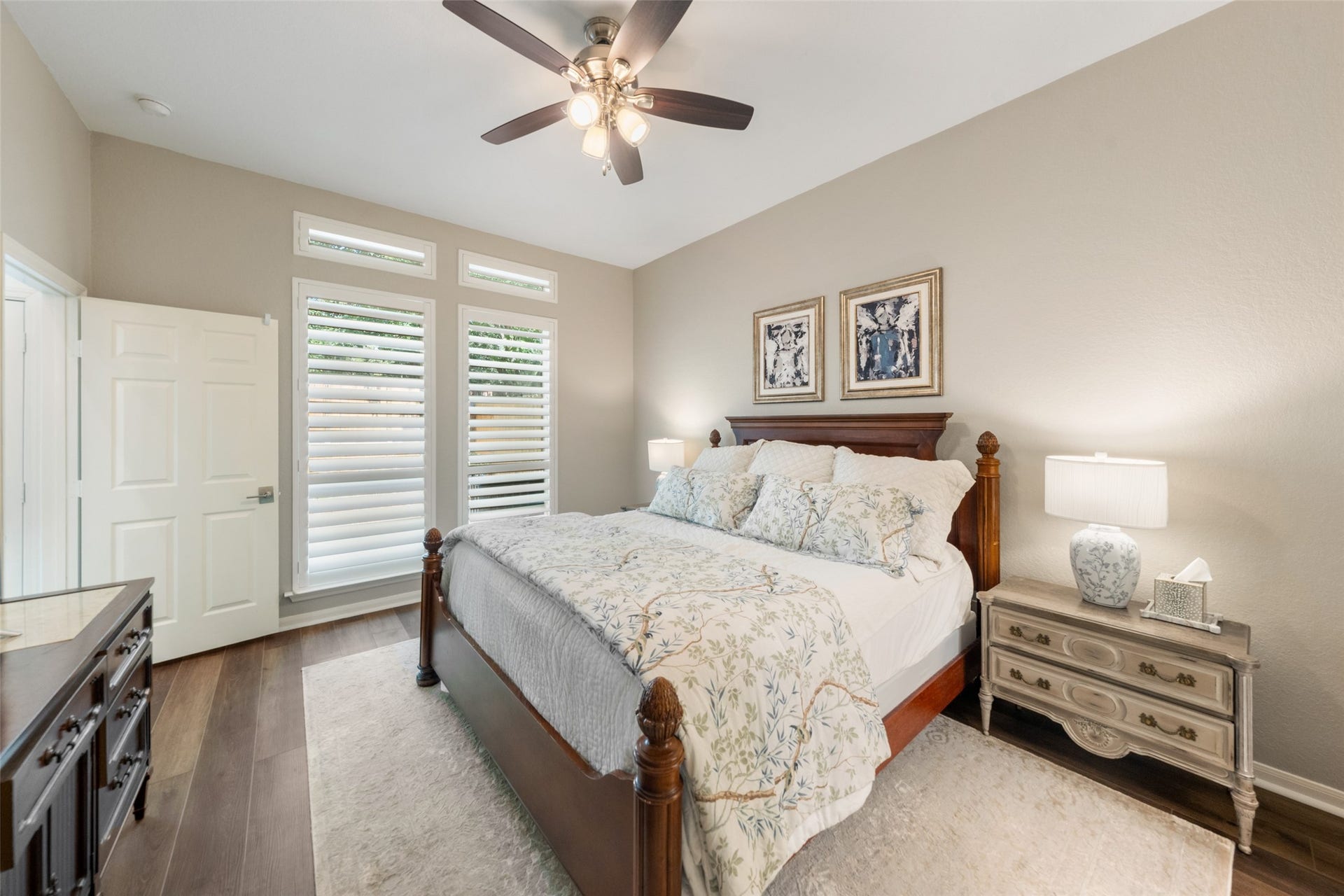 34 Alderon Woods Place, The Woodlands, TX 77382 Elegant primary bedroom downstairs with warm tones features abundant natural light through tall windows with shutters.