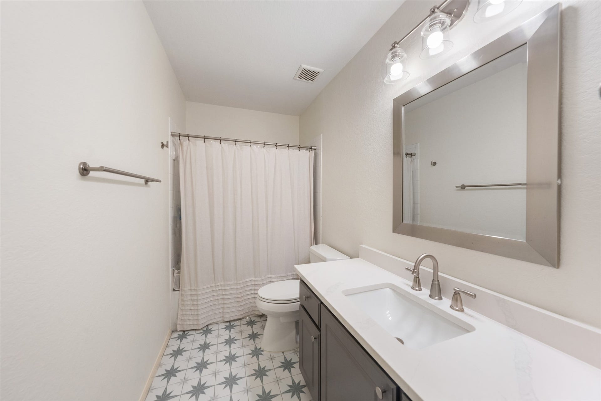 34 Alderon Woods Place, The Woodlands, TX 77382 Chic secondary bathroom featuring a sleek vanity with modern fixtures, a stylish framed mirror, and a fresh, neutral color palette complemented by a patterned tile floor.