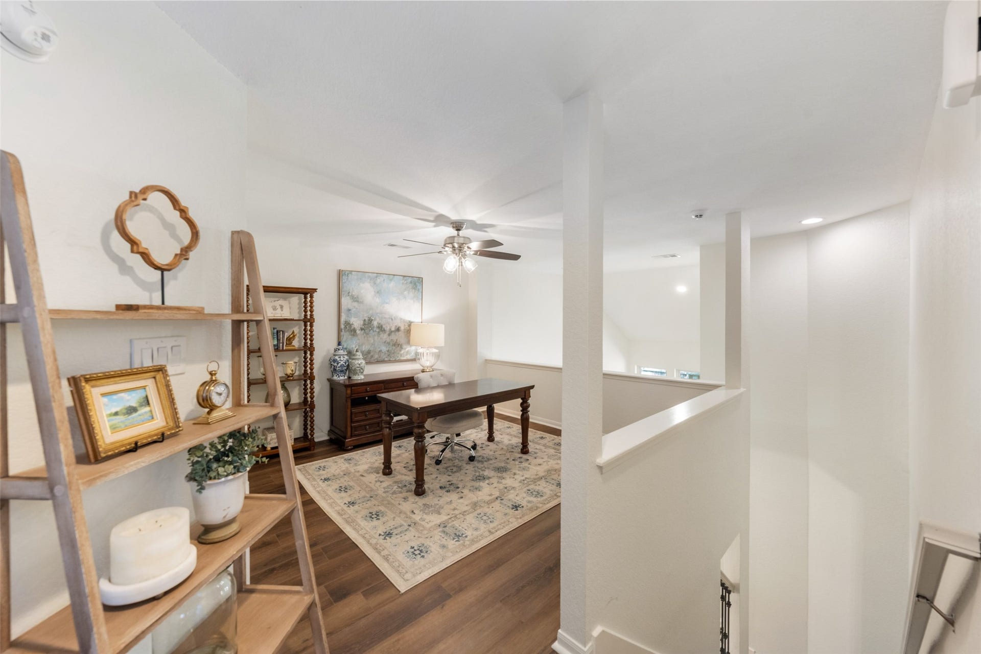 34 Alderon Woods Place, The Woodlands, TX 77382 Bright and inviting loft space with a stylish home office setup, featuring a ceiling fan, elegant shelving, and a cozy area rug on beautiful flooring.