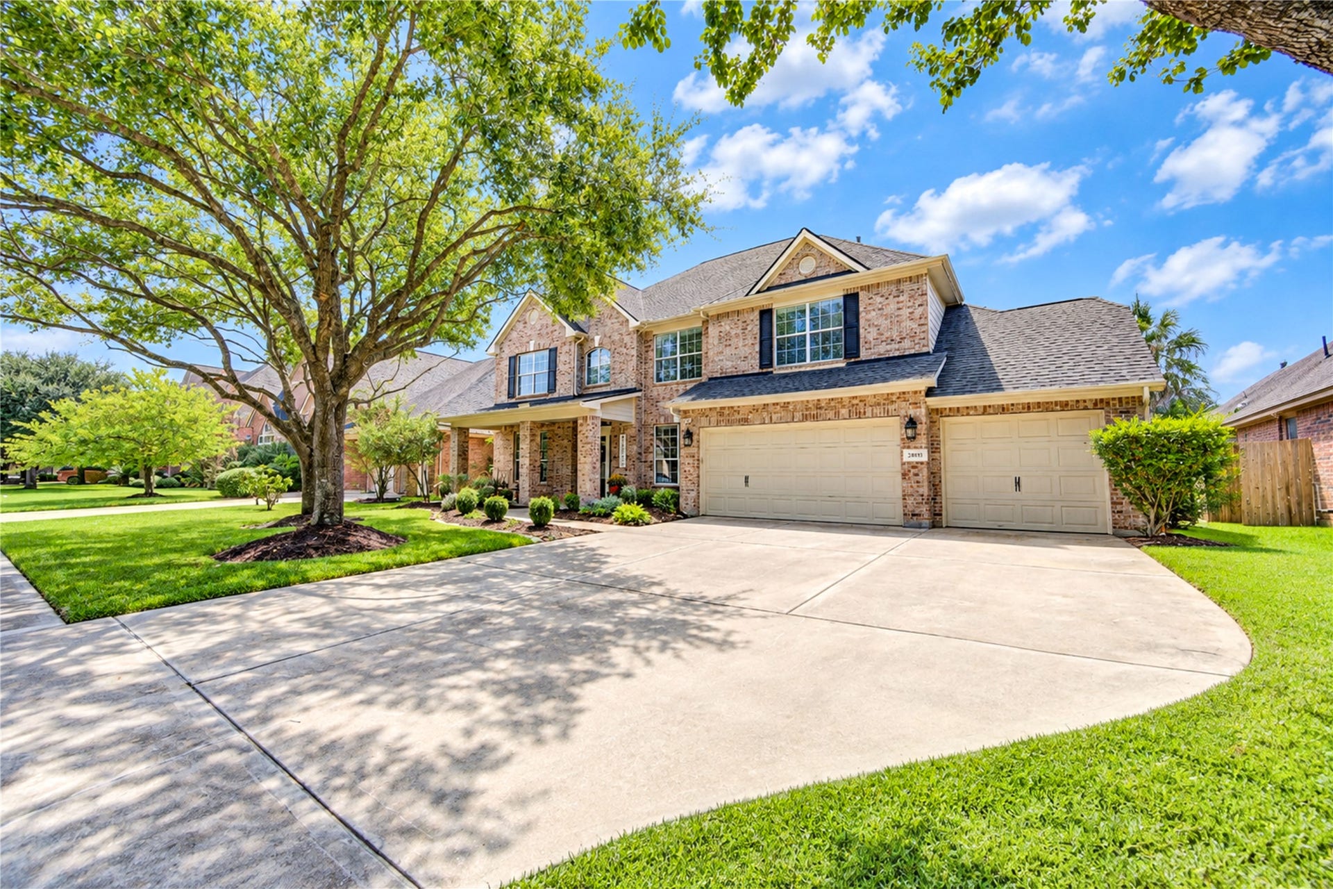 28019 Longspur Drive, Katy, TX 77494 3 car garage with large oak tree and beds with plants and fresh mulch.