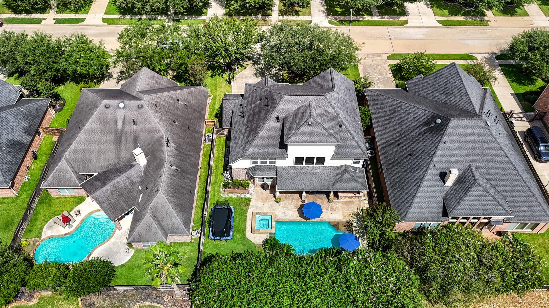 28019 Longspur Drive, Katy, TX 77494 Drone shot of backyard with home, pool with blue umbrellas and trampoline.