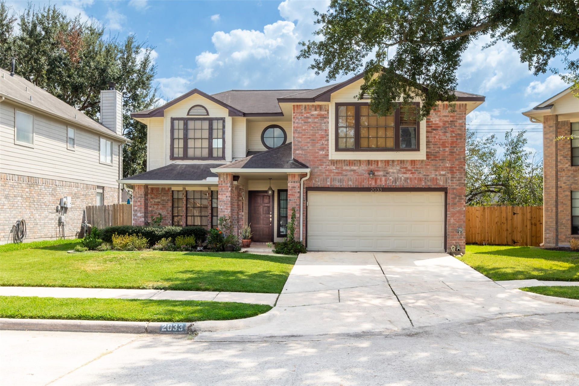 2033 Wildwood Ridge Drive, Missouri City, TX 77489 Beautiful curb appeal featuring a traditional multi-level roofline, multi-pane accent windows including a distinctive round architectural window, an expansive driveway, and a vibrant green lawn.