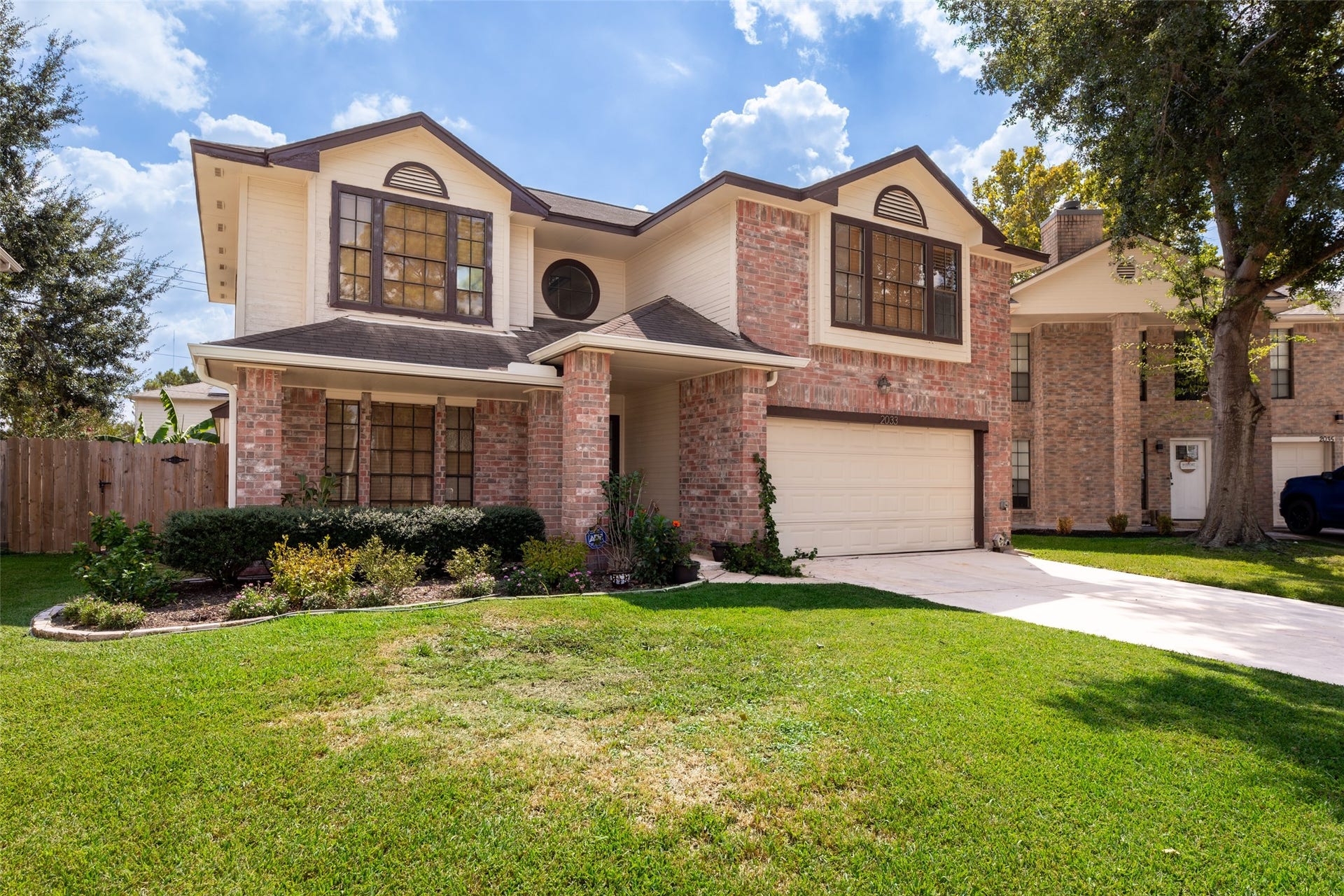 2033 Wildwood Ridge Drive, Missouri City, TX 77489 Charming front exterior showcasing a classic brick and neutral siding facade, a welcoming covered entryway, a spacious two-car garage, and a neatly manicured front lawn shaded by mature trees.