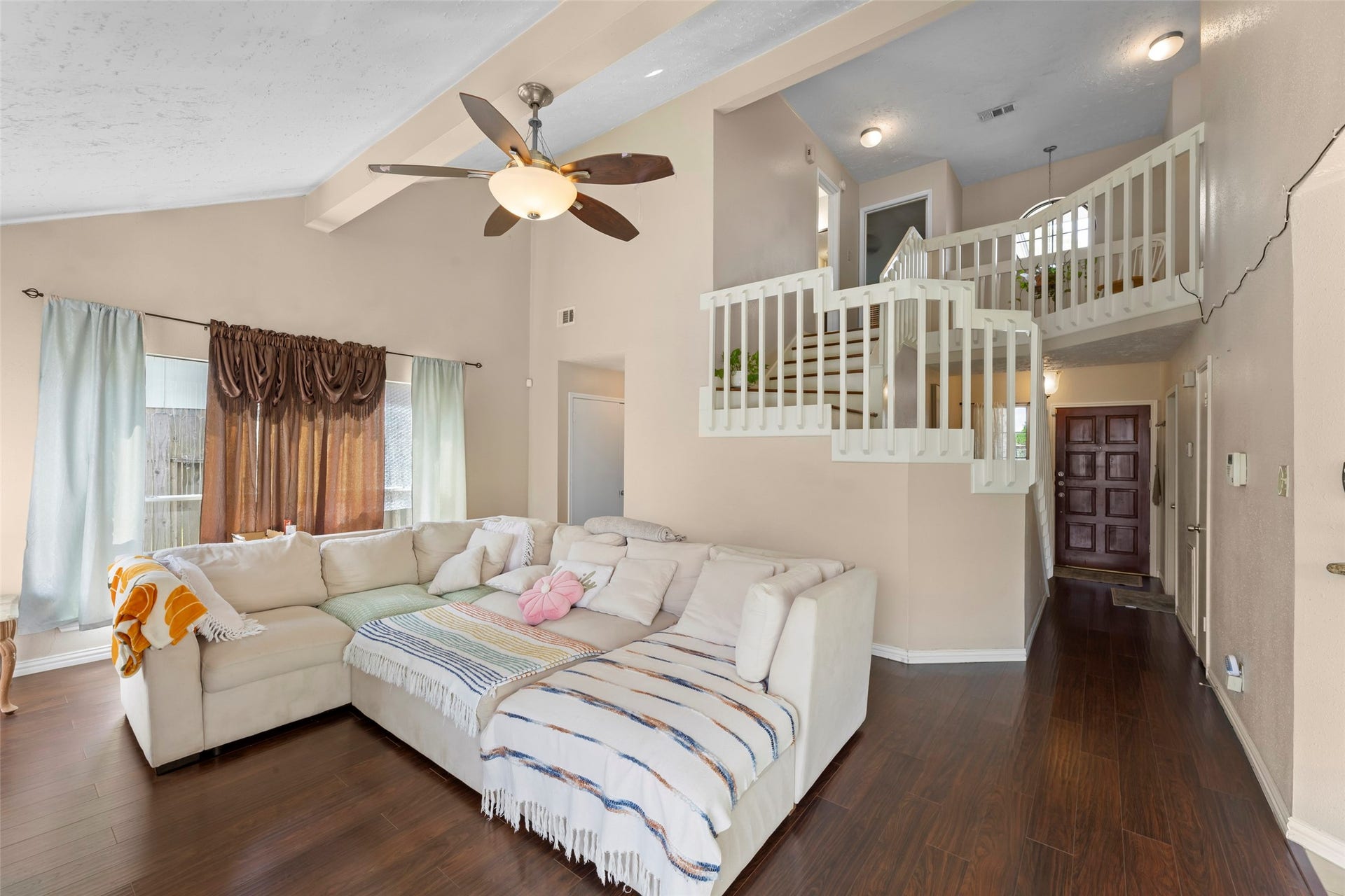 2033 Wildwood Ridge Drive, Missouri City, TX 77489 With plenty of natural lighting, this open living room highlighting dark wood flooring, high vaulted ceilings, a central brick fireplace, and large windows with integrated blinds.