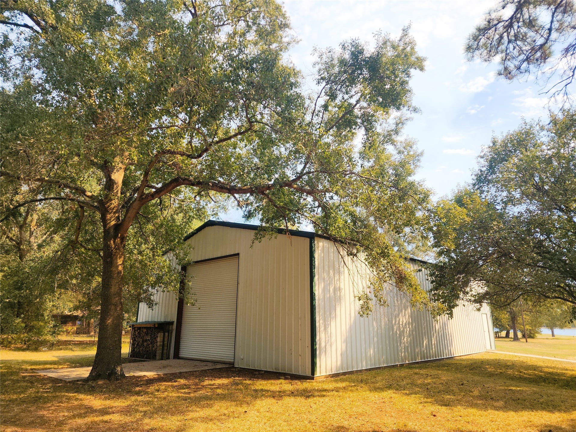 557 Fm 2693 Road E, New Waverly, TX 77358 Spacious metal building with a large roll-up door, nestled among mature trees on a serene property.