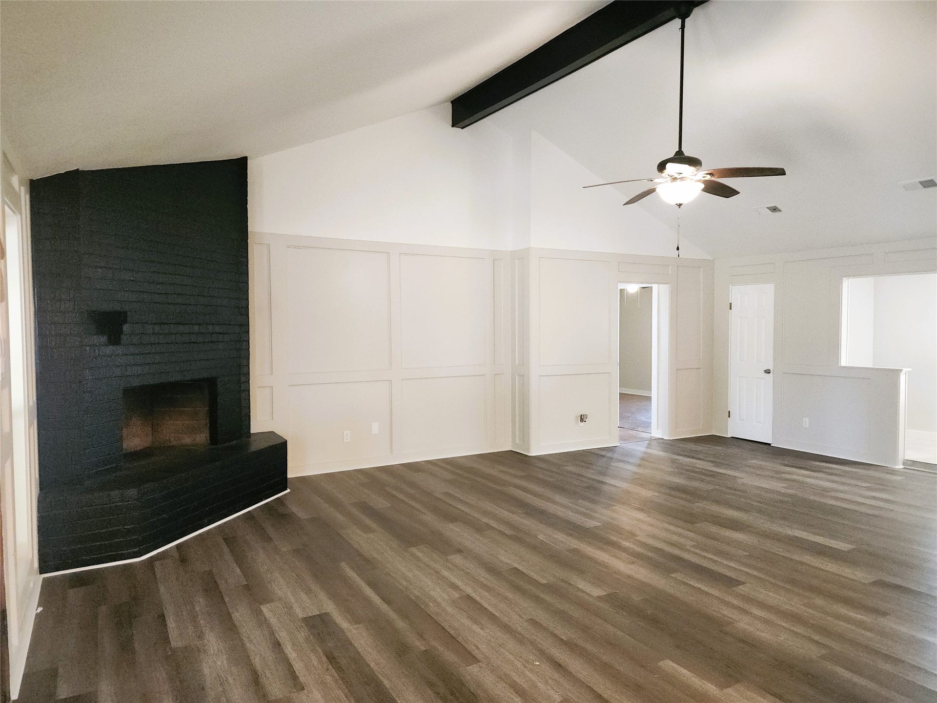 557 Fm 2693 Road E, New Waverly, TX 77358 Spacious living room featuring a striking black brick fireplace, vaulted ceilings with exposed beams, and elegant wood-look flooring for a modern and inviting atmosphere.