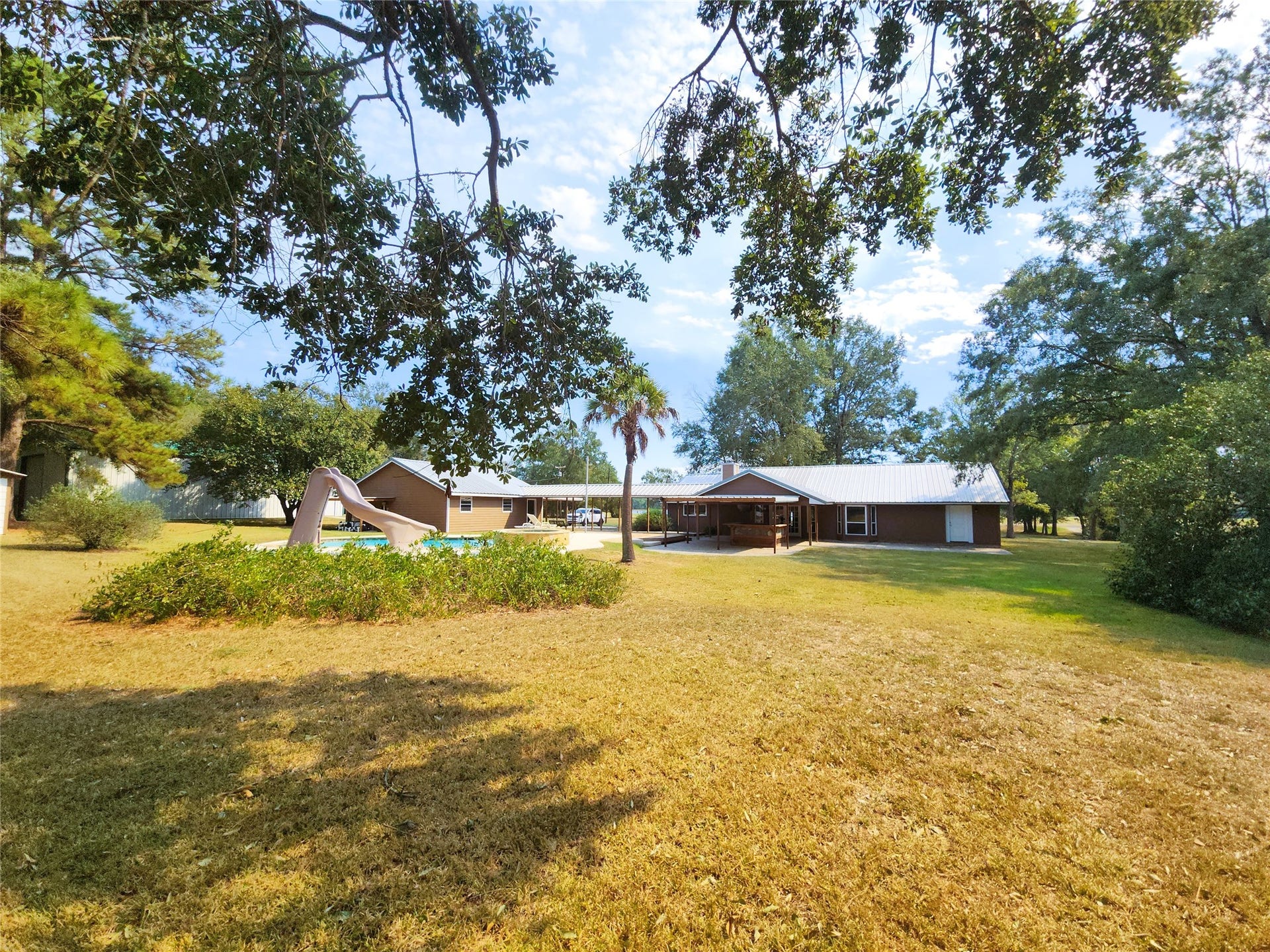 557 Fm 2693 Road E, New Waverly, TX 77358 Expansive backyard featuring a charming home with a metal roof, surrounded by mature trees and a private pool with a slide, perfect for outdoor enjoyment.