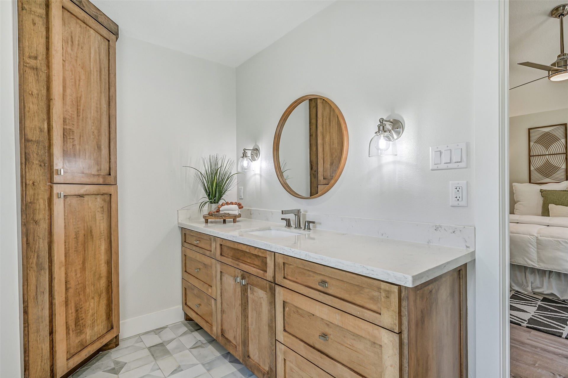 921 Falling Leaf Drive, Friendswood, TX 77546 The beautifully redesigned primary bath features a 7' quartz vanity with abundant stained cabinetry, designer marble-look patterned tile flooring, contemporary sconces & a round wood-framed mirror, plus additional tall cabinetry for impressive bathroom storage.