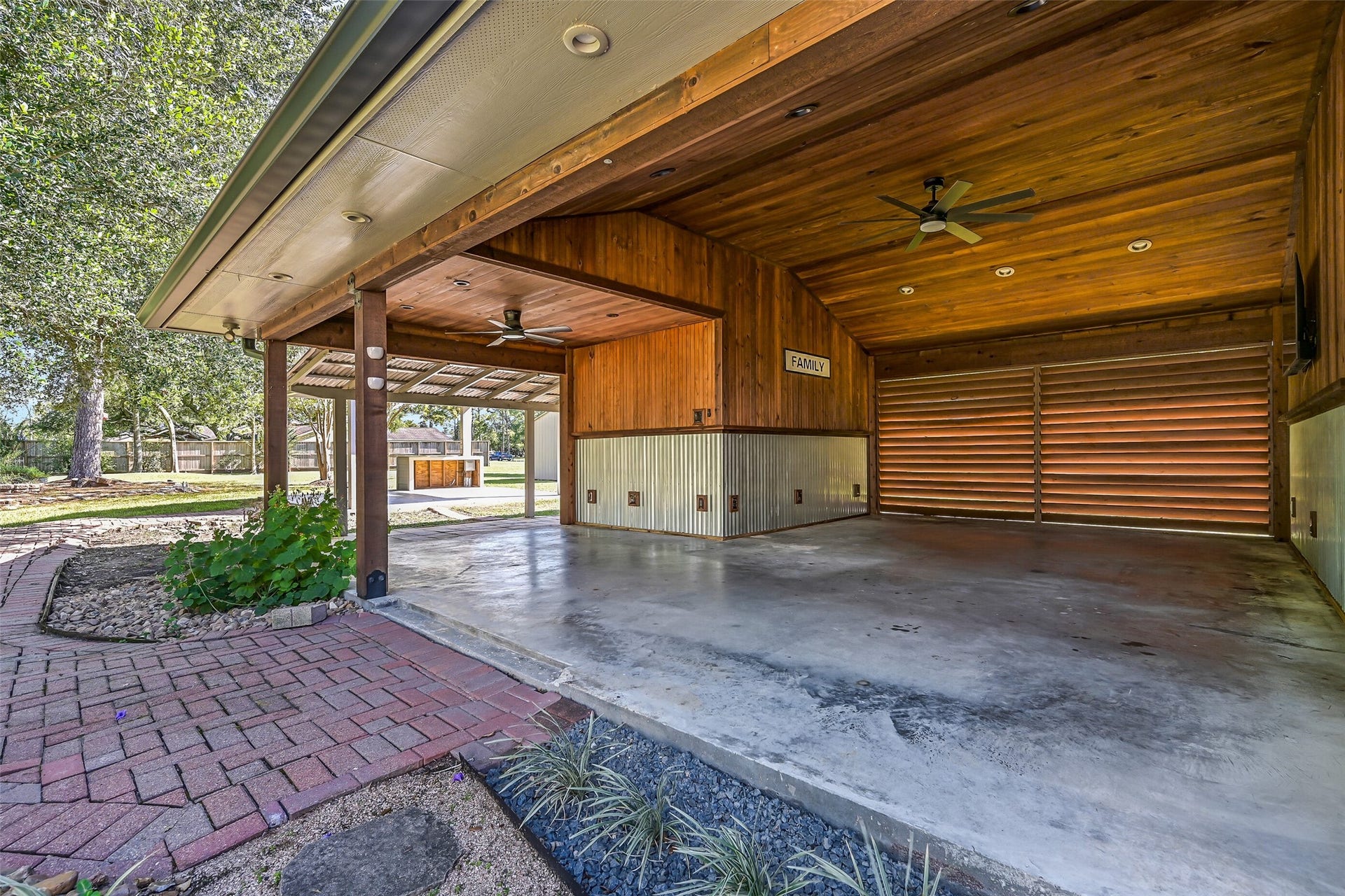 921 Falling Leaf Drive, Friendswood, TX 77546 Another view reveals the impressive scale of the L-shaped covered patio behind the garage, with slatted wood screening, corrugated metal accents, multiple ceiling fans & abundant electrical. A rear-access storage bay provides convenient space for lawn equipment.
