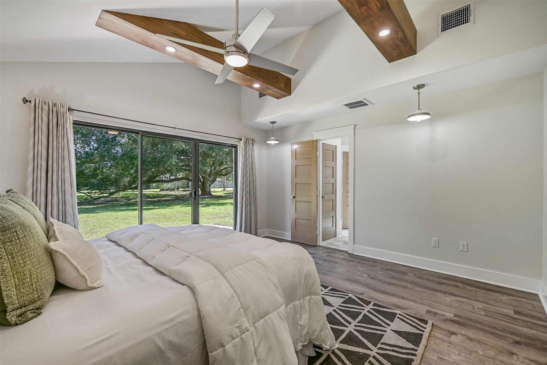 921 Falling Leaf Drive, Friendswood, TX 77546 Another view highlights the architectural character of the vaulted primary suite, where substantial cedar beams add warmth overhead and triple sliding glass doors frame a beautiful view of the magnificent century oak and park-like grounds.