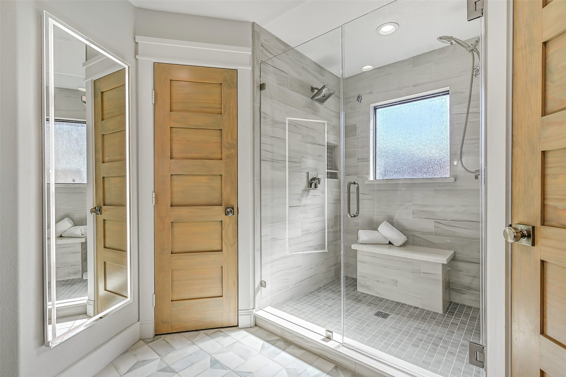 921 Falling Leaf Drive, Friendswood, TX 77546 An oversized seamless-glass shower creates a spa-like focal point with floor-to-ceiling wood-look tile, built-in bench, dual showerheads & privacy window. A full-length illuminated mirror, private water closet and separate his & hers closets with built-ins complete the primary bath.