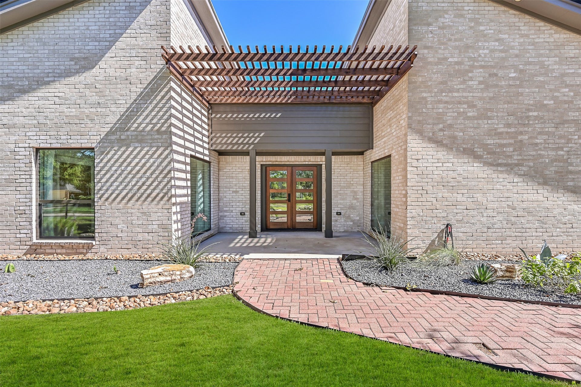 921 Falling Leaf Drive, Friendswood, TX 77546 A dramatic recessed entry makes a memorable first impression with a wood pergola, modern landscaping, oversized black-framed windows & handsome double wood-and-glass doorsa fitting introduction to this completely redesigned home.