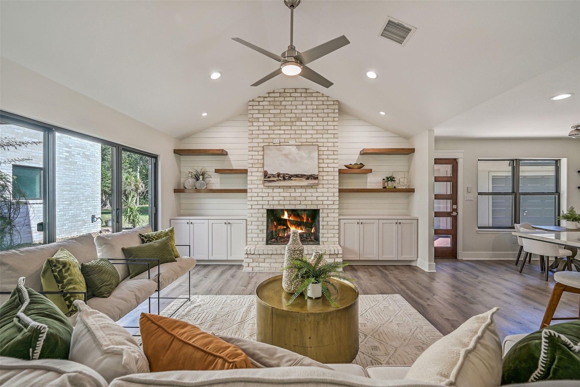 921 Falling Leaf Drive, Friendswood, TX 77546 A soaring cream colored brick wood-burning fireplace anchors the vaulted family room, flanked by custom built-ins with shiplap detailing, stained floating shelves & abundant closed storage. Recessed lighting and a modern ceiling fan complete the contemporary space.