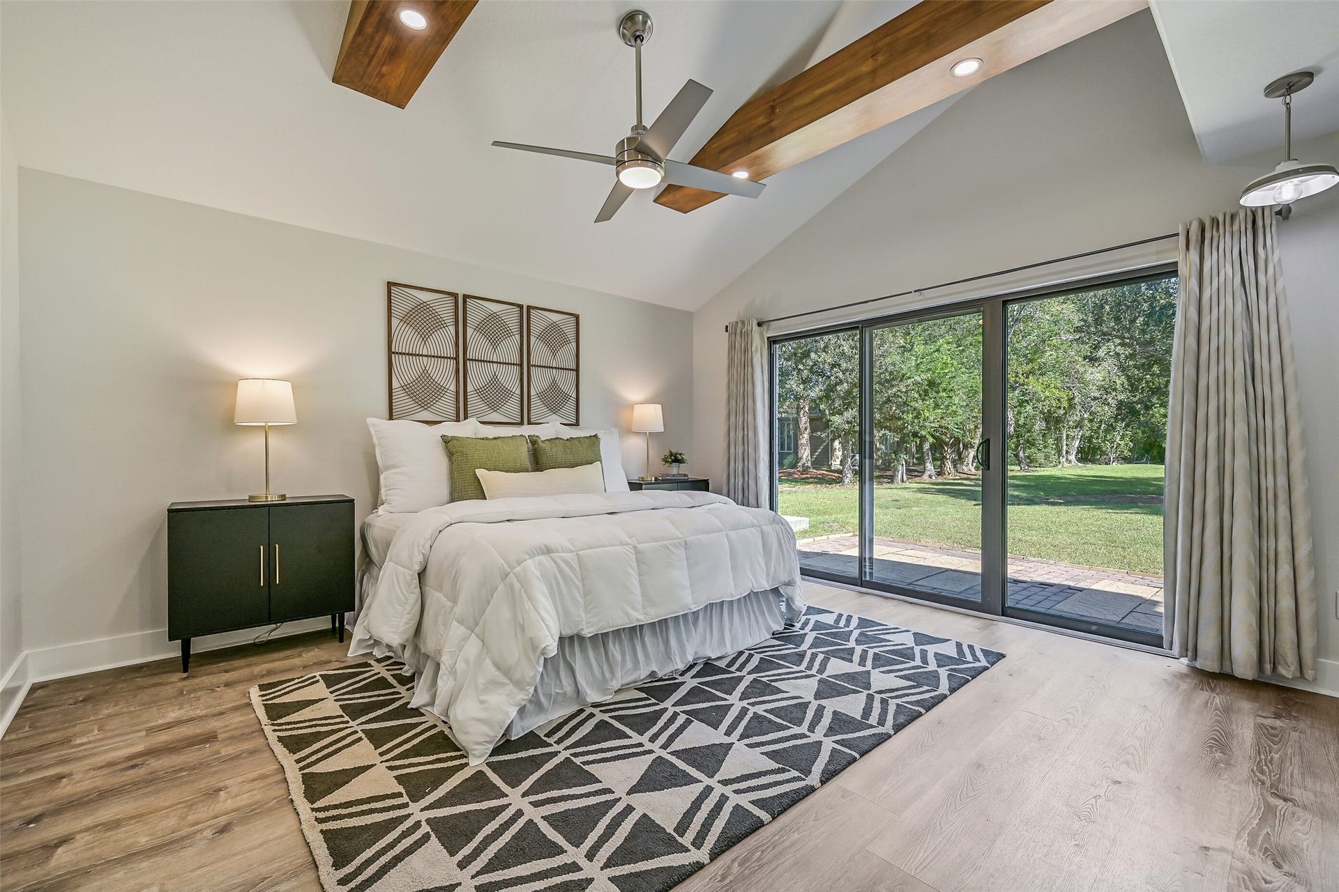 921 Falling Leaf Drive, Friendswood, TX 77546 The 15' x 14' primary retreat showcases a dramatic vaulted ceiling with stained cedar beams, integrated recessed lighting, a modern lighted ceiling fan & luxury vinyl plank floors. Triple sliding glass doors open directly to the terrace and expansive backyard.