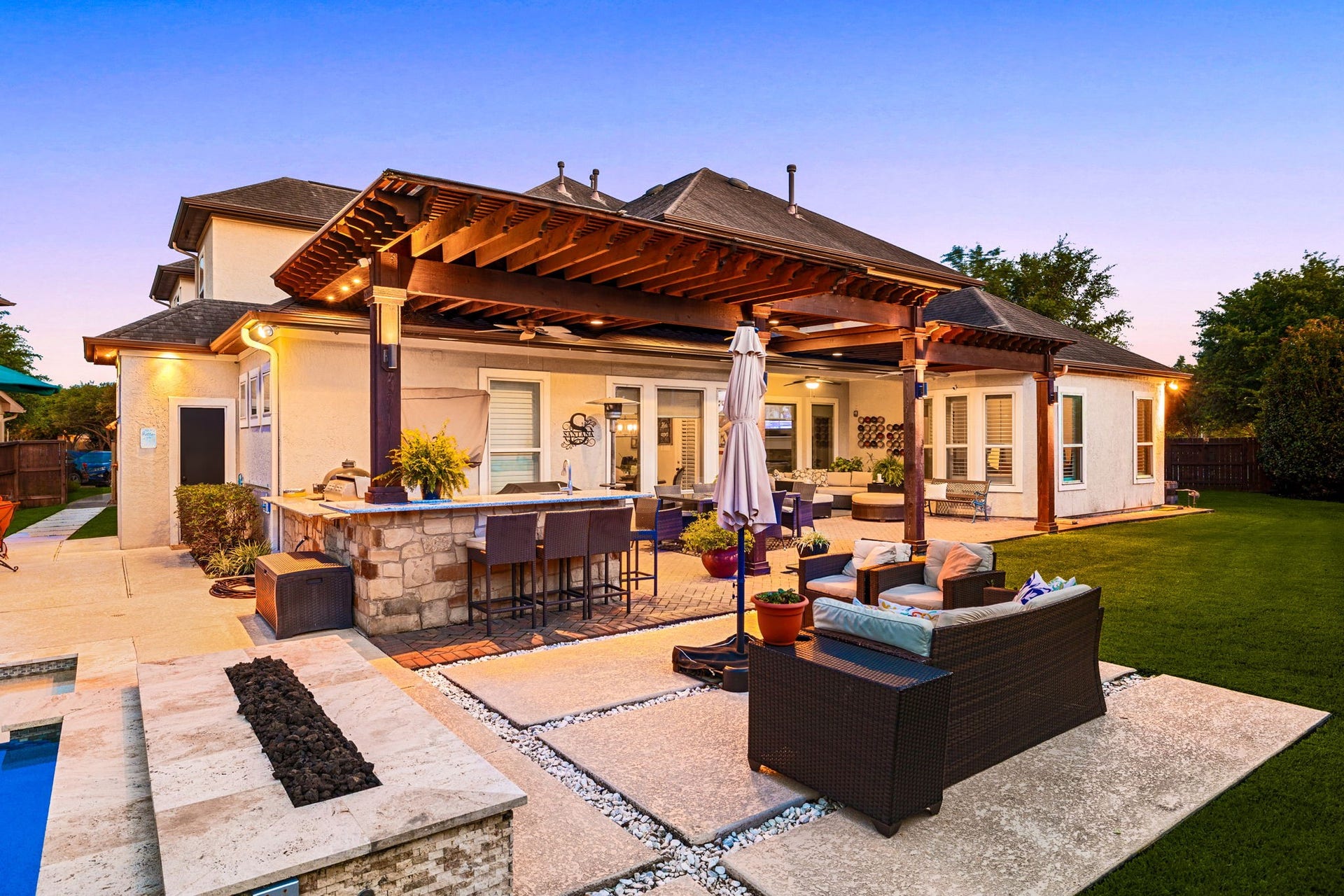 5102 Hawthorne Bend Drive, Katy, TX 77494 Backyard goals at golden hour! This breathtaking outdoor living space features a grand wood pergola with recessed lighting, a stacked stone outdoor kitchen and bar, built-in fire feature, travertine and brick paver patio, and lush green lawn, the ultimate entertainer's dream under the Texas sky!