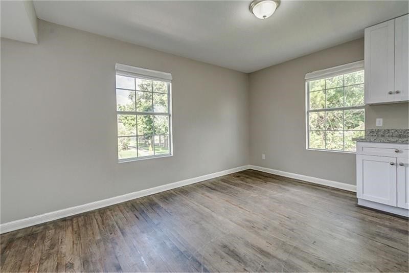 3502 Rosedale Street, Houston, TX 77004 Inviting room with large windows, sleek hardwood flooring, and a glimpse of a modern kitchen area featuring white cabinetry.