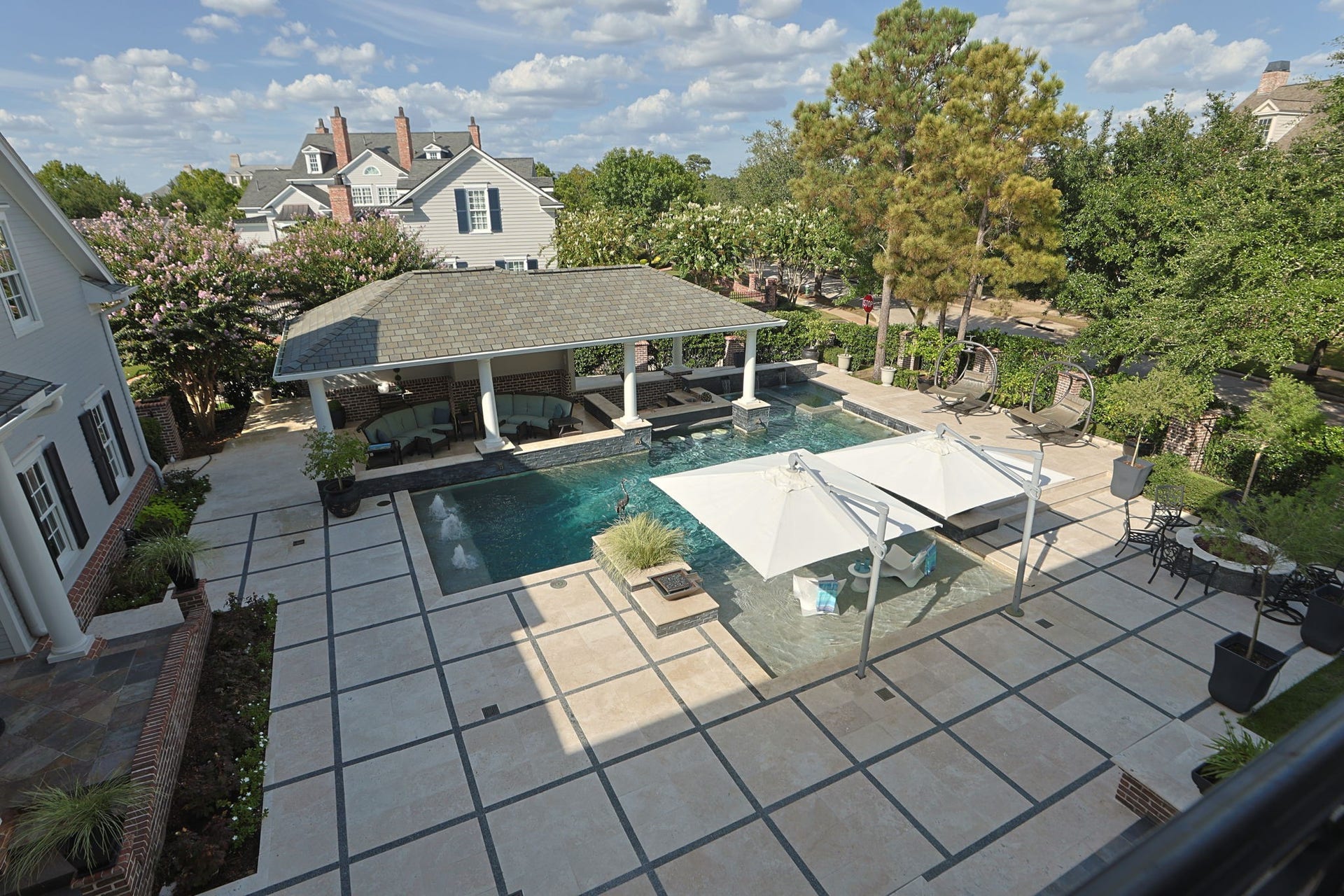 2 Georgian Row, The Woodlands, TX 77380 A commanding view from the upper veranda showcases the extraordinary scale and design of the backyard retreat. The custom pool anchors an expansive stone courtyard with integrated water features, generous lounging areas, lush landscaping, and a substantial covered pavilion created for year-round outdoor entertaining.