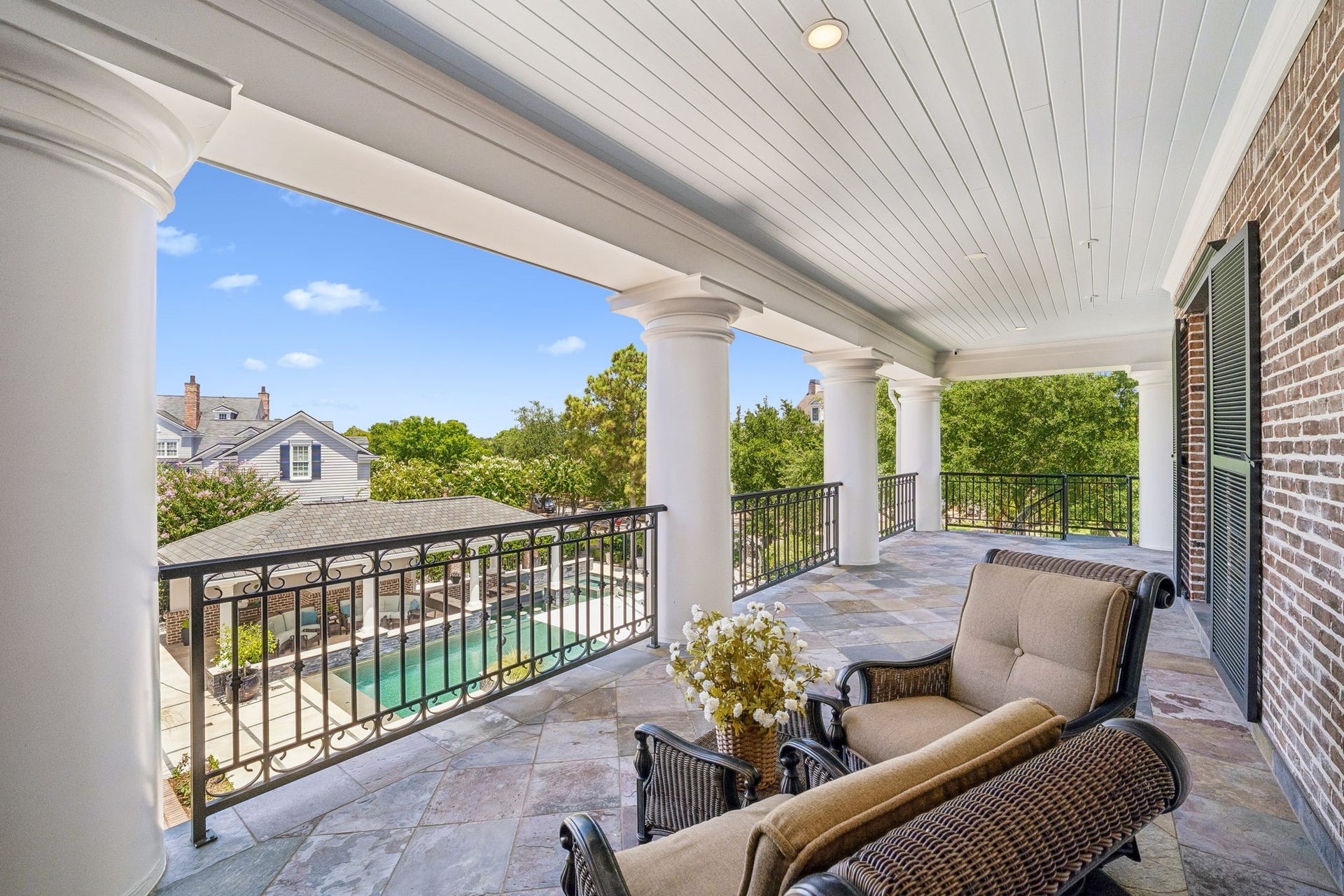 2 Georgian Row, The Woodlands, TX 77380 Beautiful covered veranda overlooking the pool and outdoor entertaining areas, featuring slate tile flooring, classic columns, wrought-iron railings, recessed lighting, and plenty of room for comfortable outdoor seating.
