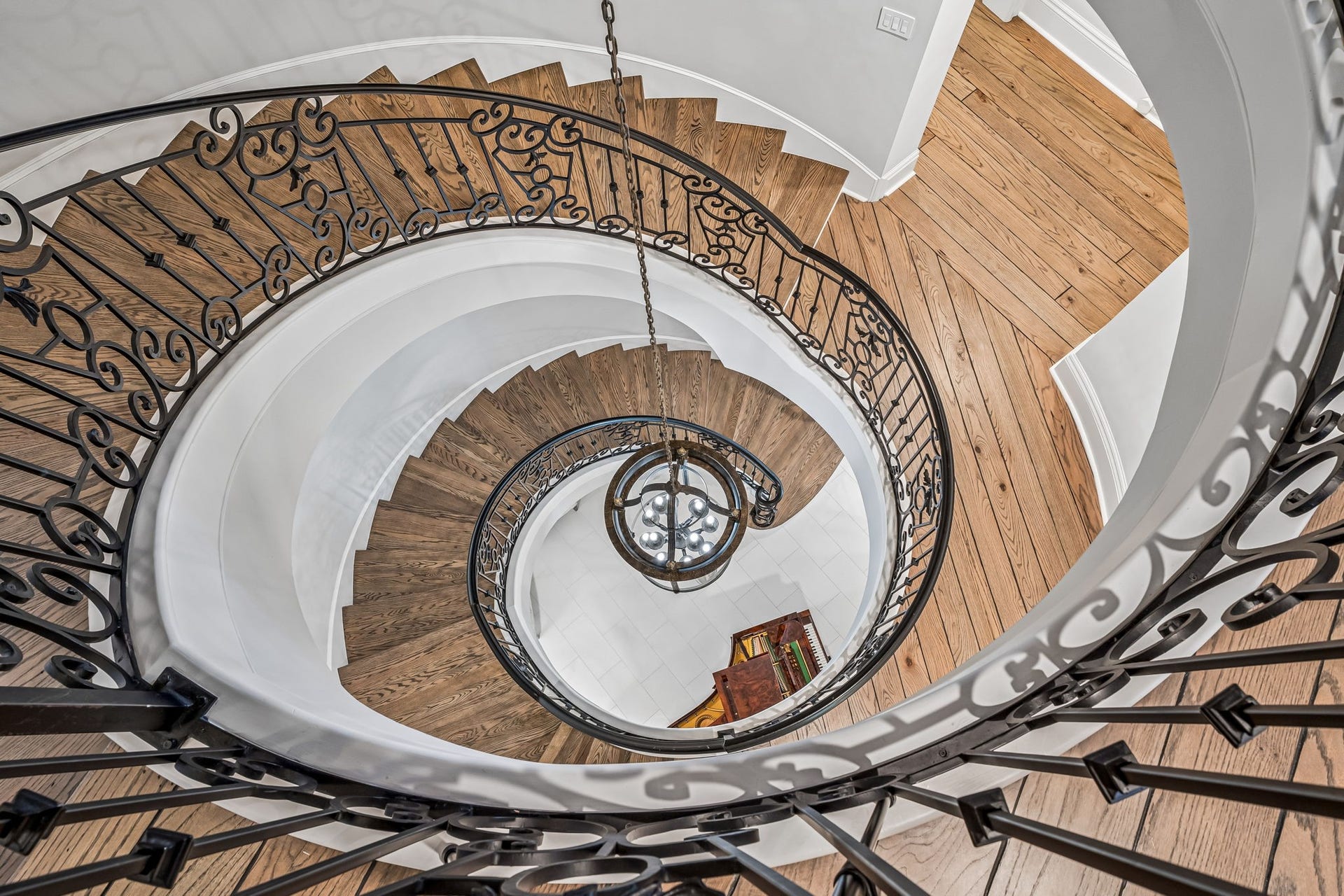 2 Georgian Row, The Woodlands, TX 77380 A dramatic view from above showcases the graceful curves and intricate ironwork of the three-story spiral staircase, creating a striking architectural focal point. The chandelier is motorized for alternative positioning.