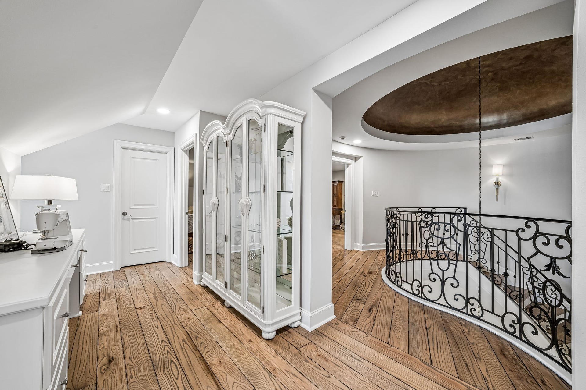 2 Georgian Row, The Woodlands, TX 77380 Third-floor landing overlooking the dramatic stairwell, showcasing the homes detailed wrought-iron railing, hardwood floors, architectural ceiling detail, and spacious layout connecting the upstairs living areas.