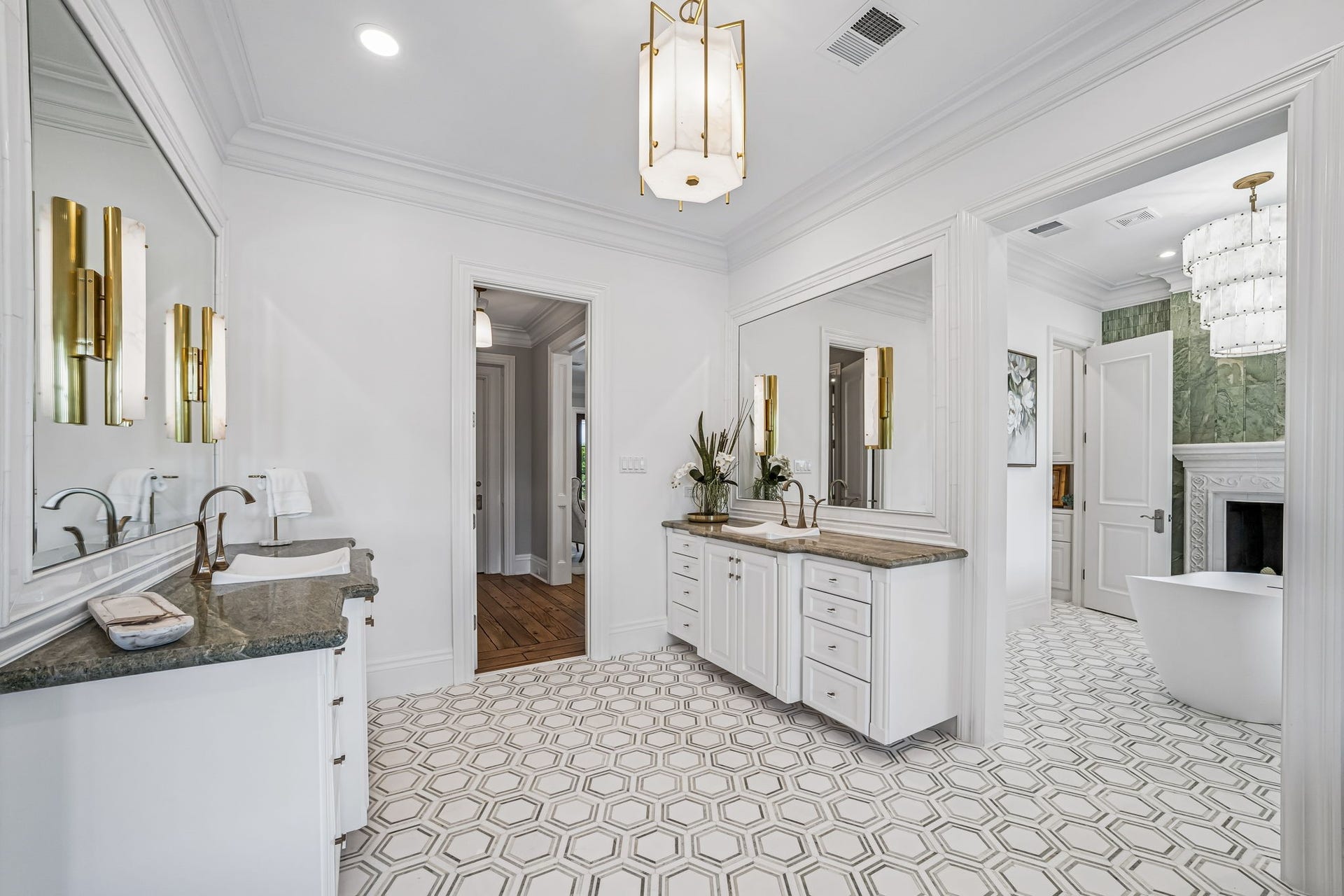2 Georgian Row, The Woodlands, TX 77380 The primary bath makes a statement from the moment you enter with separate custom vanities, oversized framed mirrors, designer lighting, detailed millwork, and intricate geometric mosaic marble flooring that continues into the freestanding tub area.