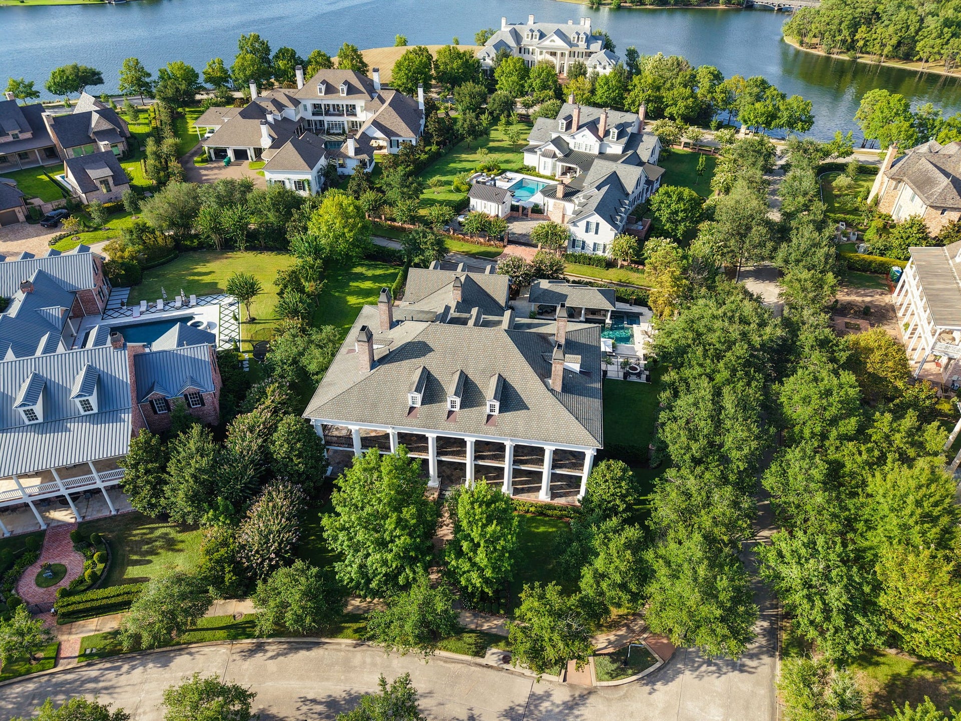 2 Georgian Row, The Woodlands, TX 77380 Surrounded by mature tree canopies and beautifully maintained grounds, with the lake just beyond the property. Notice the large side yard to the left has plenty of room for activities and play.