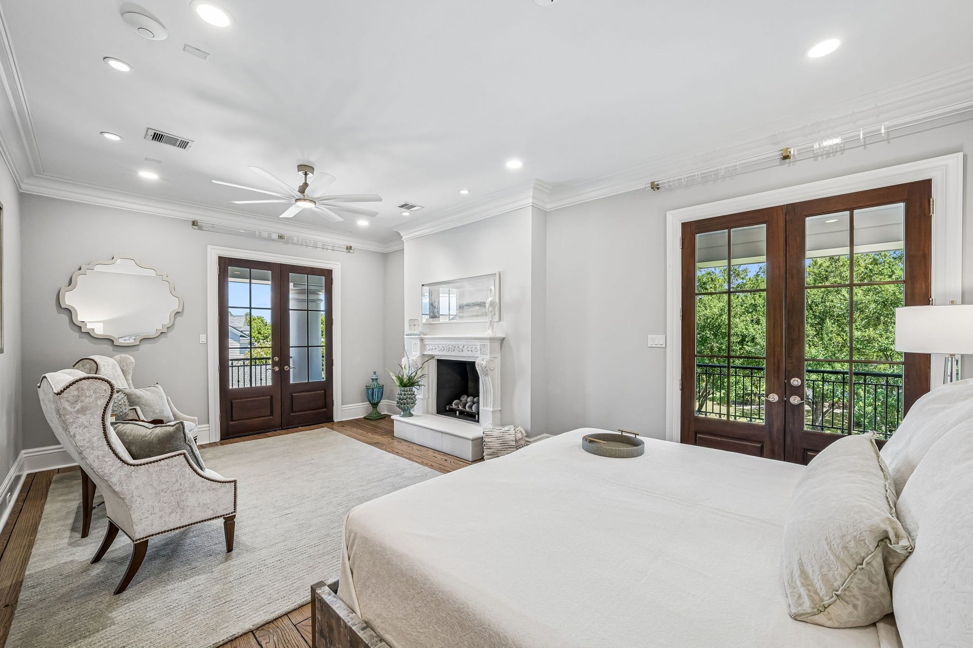 2 Georgian Row, The Woodlands, TX 77380 Expansive primary suite with hardwood flooring, detailed crown molding, recessed lighting, a private fireplace, and multiple sets of French doors that fill the room with natural light and open to the veranda but private with evergreen trees.