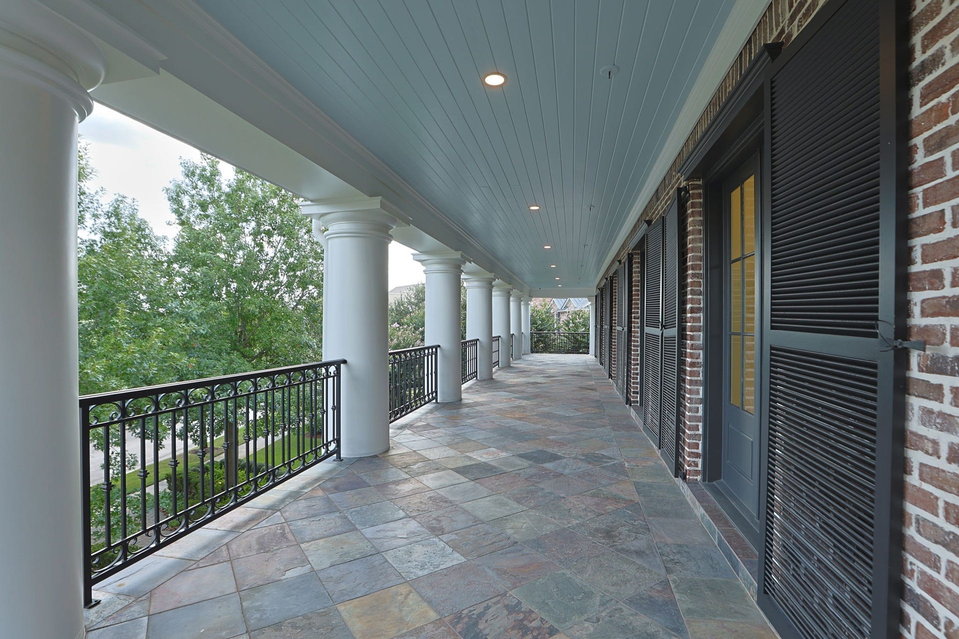 2 Georgian Row, The Woodlands, TX 77380 An impressive view of the homes expansive covered veranda, extending along the residence with slate tile flooring, stately columns, wrought-iron detailing, recessed lighting, and multiple new doors providing access from the interior. A beautiful extension of the homes living space for relaxing or entertaining outdoors.