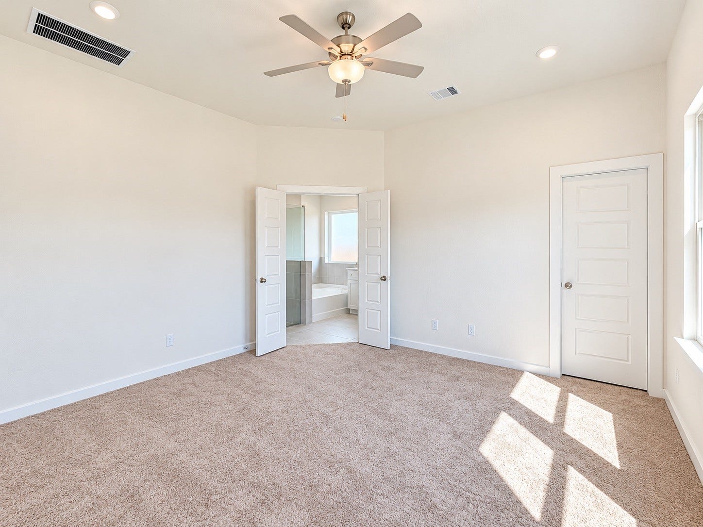 419 Pirate Falls Lane, Crosby, TX 77532 Spacious primary bedroom with plush carpeting, modern ceiling fan, and ample natural light, featuring double doors leading to an en-suite bathroom.