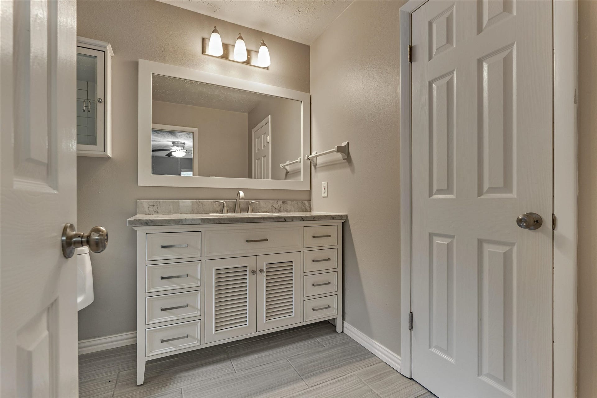 88 W White Willow Circle, The Woodlands, TX 77381 Primary bathroom with upgraded vanity with marble look composite stone coutnertop, brushed nickel faucet and hardware, framed mirror, updated lighting, and tile floors. Door on right goes into walk-in closet.
