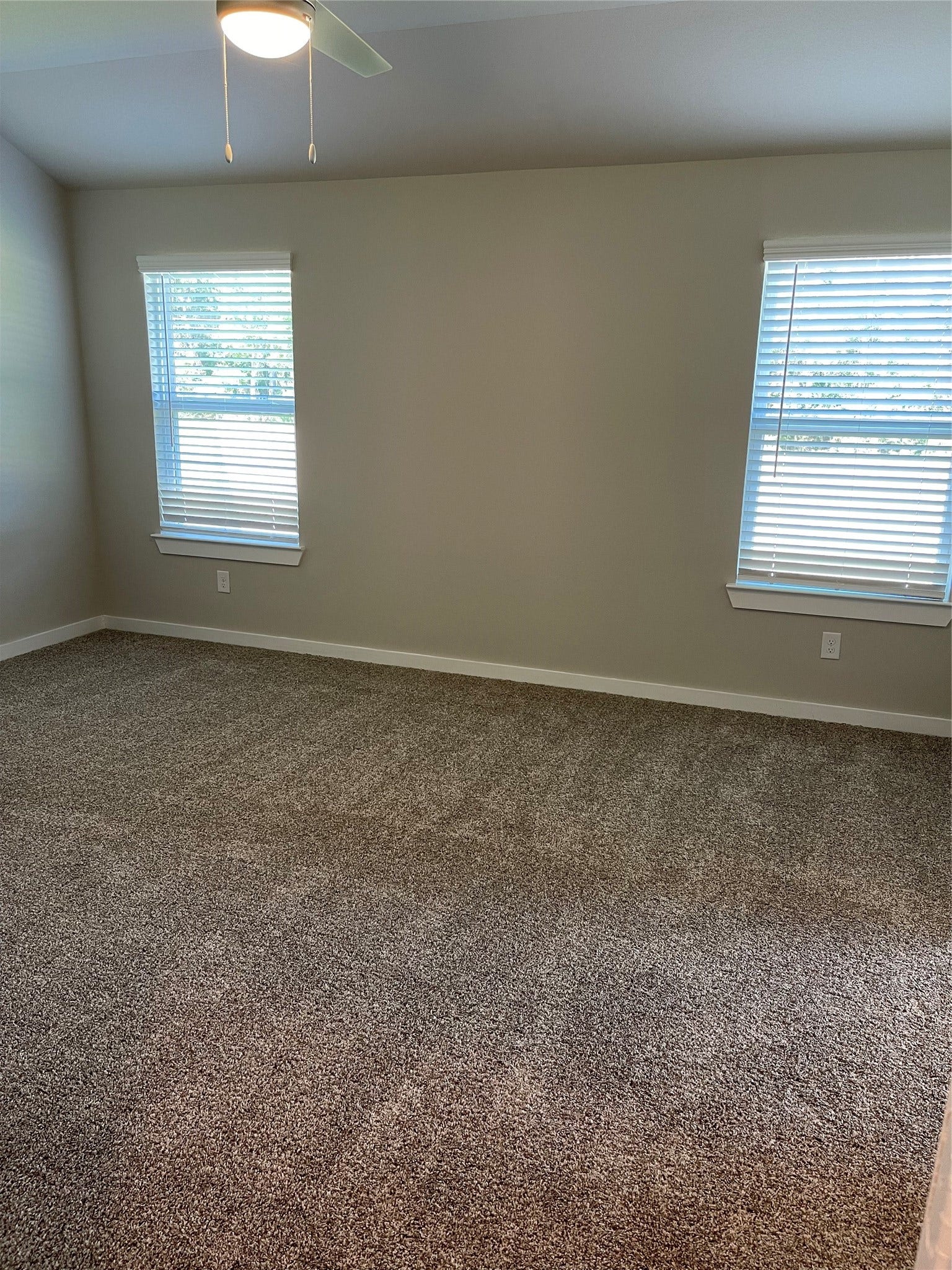 12285 Council Grove Drive, Conroe, TX 77384 Spacious carpeted room with two large windows offering ample natural light and a ceiling fan for comfort.