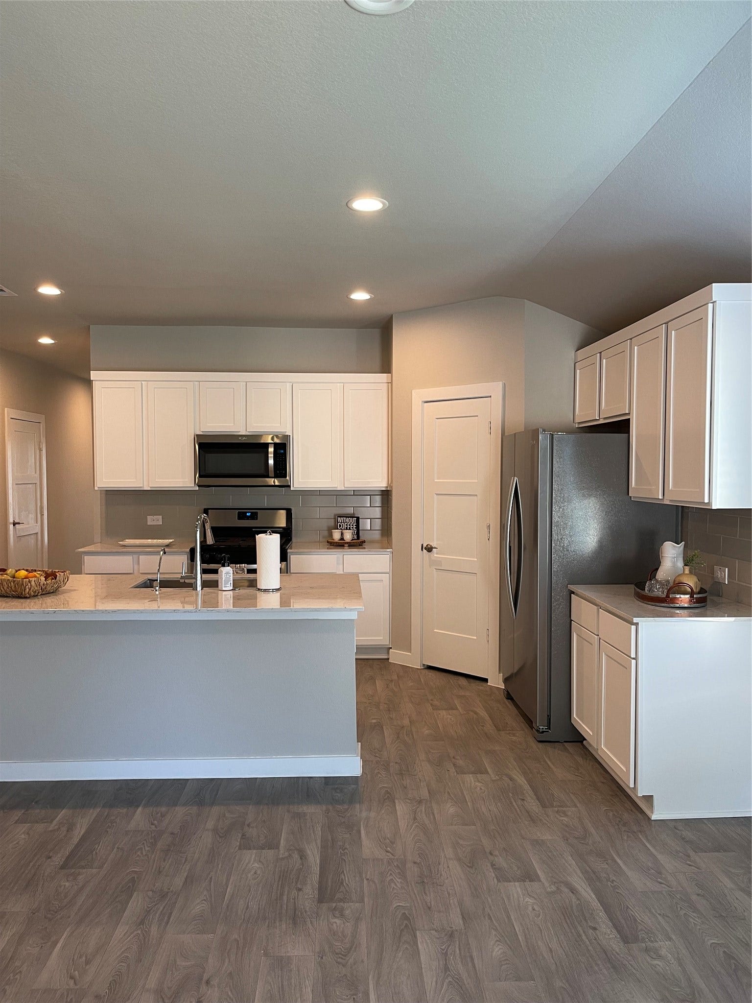 12285 Council Grove Drive, Conroe, TX 77384 Modern kitchen with sleek white cabinetry, stainless steel appliances, and a spacious island, complemented by elegant vinyl plank flooring.