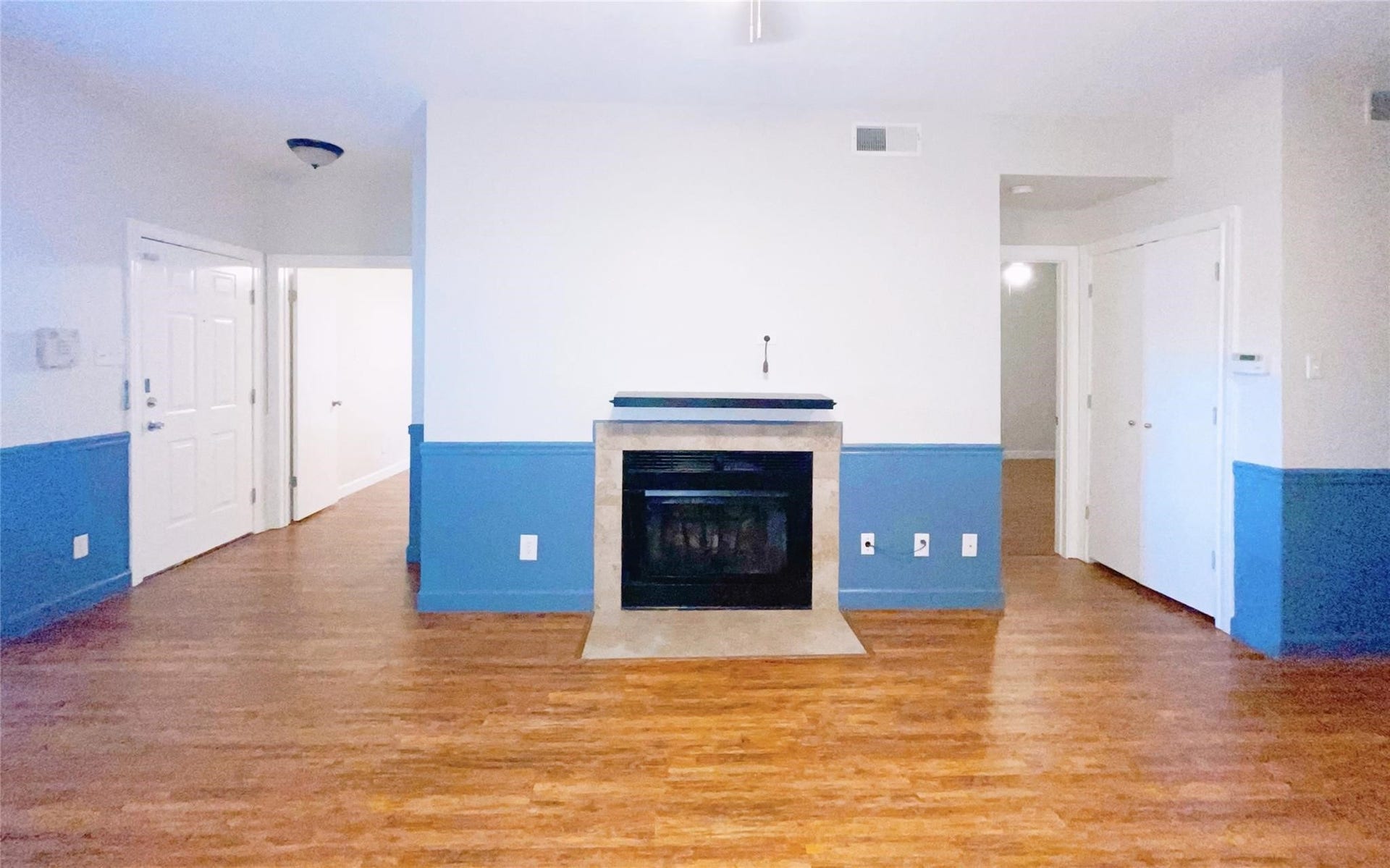 2121 El Paseo Street, #1511, Houston, TX 77054 Spacious living area featuring warm wood-look flooring, a fireplace with stone surround, and attractive blue-gray wainscoting. The open layout provides a comfortable gathering space with convenient access to the adjoining areas of the home.