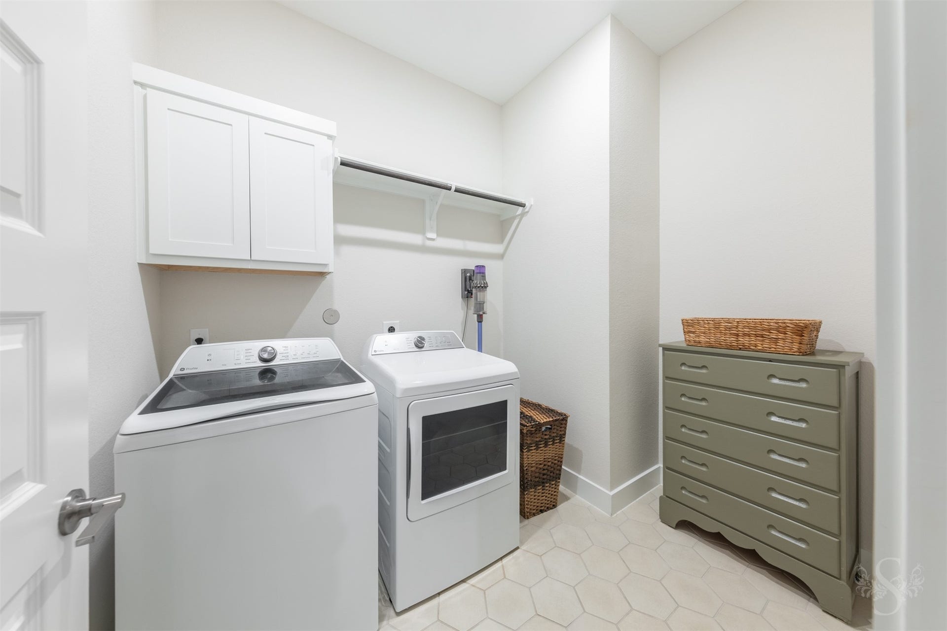 Spacious utility room offers upper cabinetry, a hanging rod and ample room for additional storage. Modern hexagon tile flooring adds a stylish finishing touch.