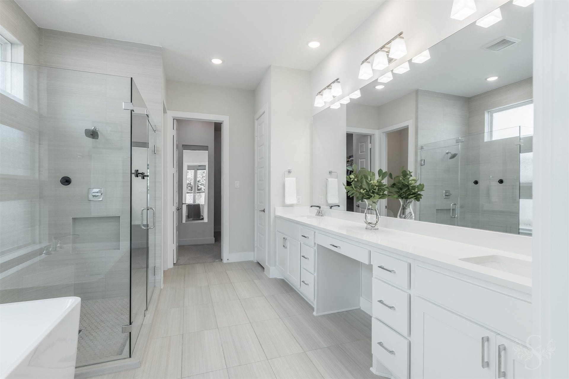 Luxurious primary bath features an extended dual quartz vanity with abundant cabinetry and an oversized frameless glass shower. Soft neutral finishes give the space a serene, spa-inspired feel.