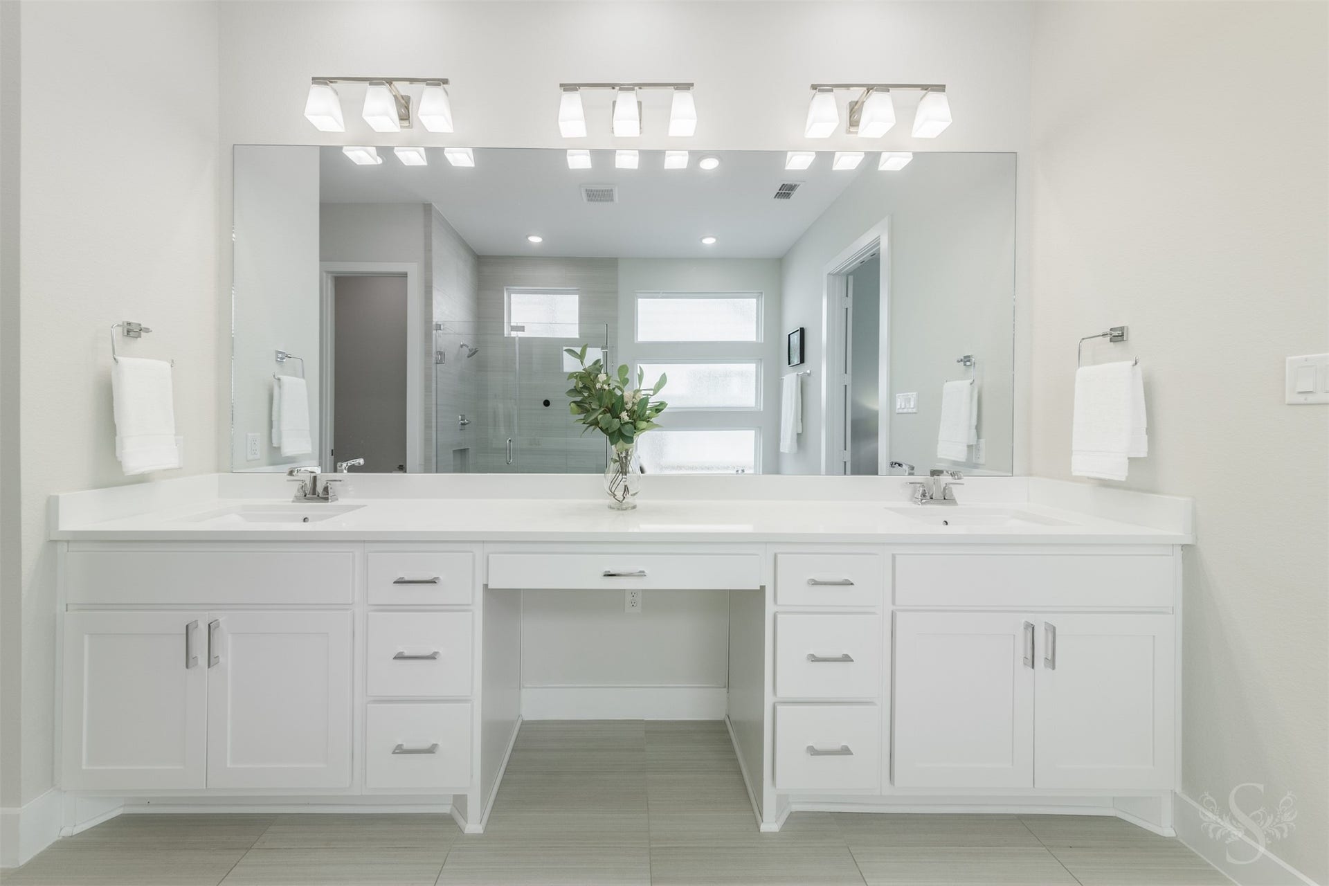 Expansive dual vanity offers abundant counter space, extensive storage and a dedicated seated makeup area. An oversized mirror and modern lighting complete this beautifully appointed primary bath.