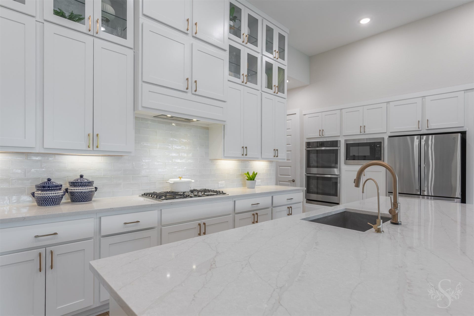 The impressive quartz island offers abundant workspace and includes a large undermount sink with designer fixtures. Towering cabinetry, glass-front displays and a statement backsplash give this kitchen incredible style.