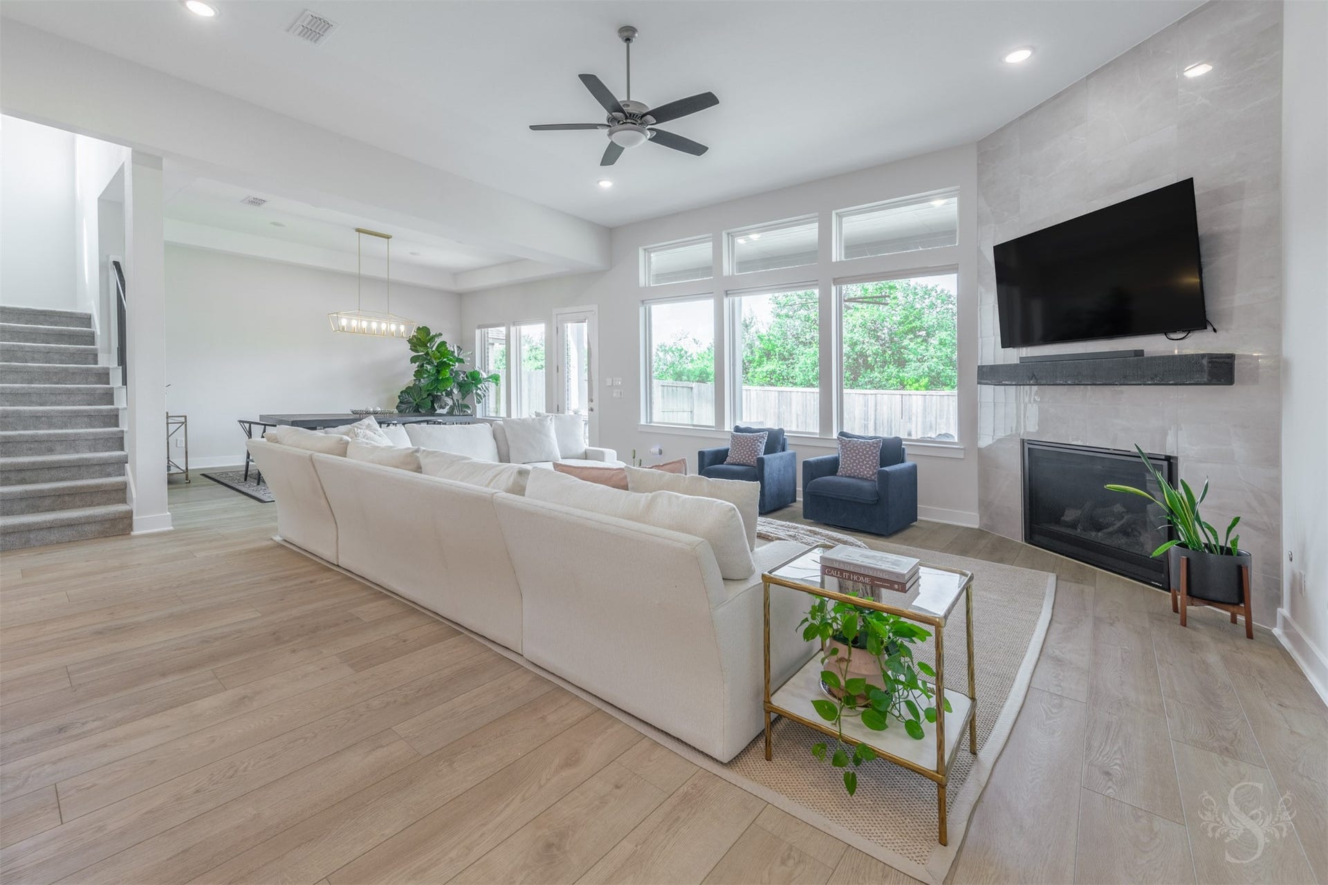 The expansive family room is centered around a dramatic floor-to-ceiling tiled fireplace with a striking floating mantel. A wall of windows fills the space with natural light and showcases views of the backyard.